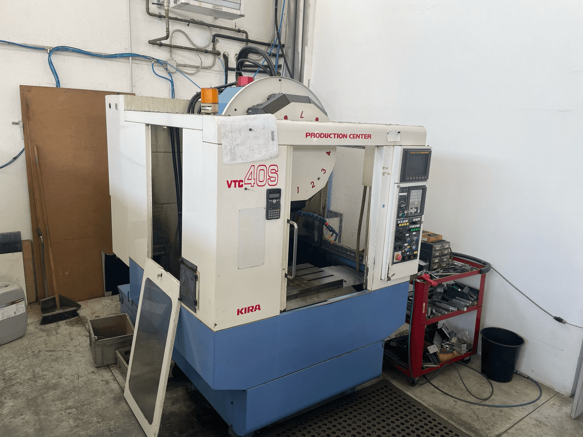 KIRA VTC 40S töötluskeskus külgvaates, millel on juhtpaneel, avatud uks ja tööriistad lähedal asuval hoiukärul.