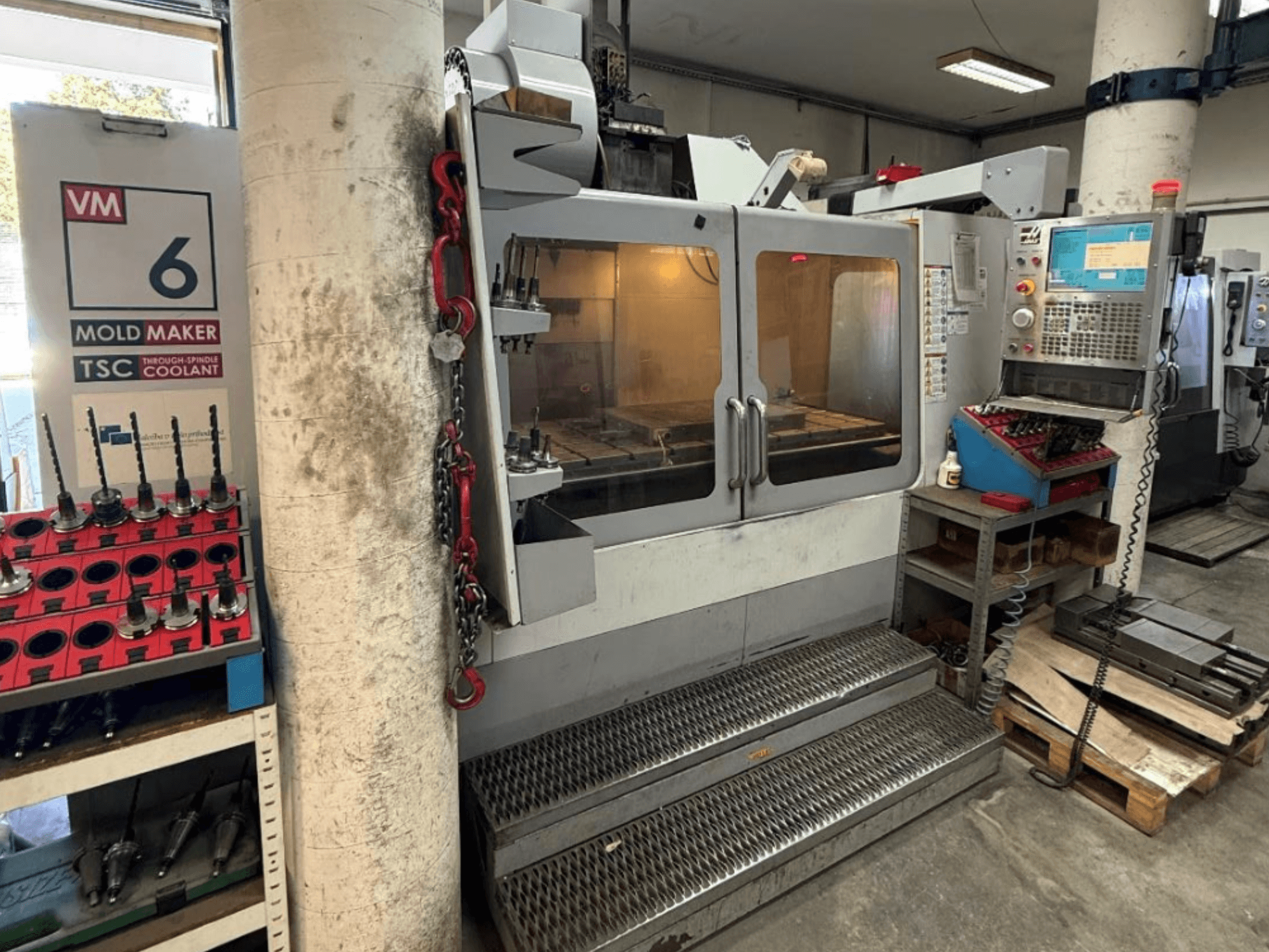 HAAS VM-6 HE vertikaalne töötlemiskeskus eestvaates, millel on näha juhtpaneel, jahutussüsteem ja tööriistade hoiuruum.