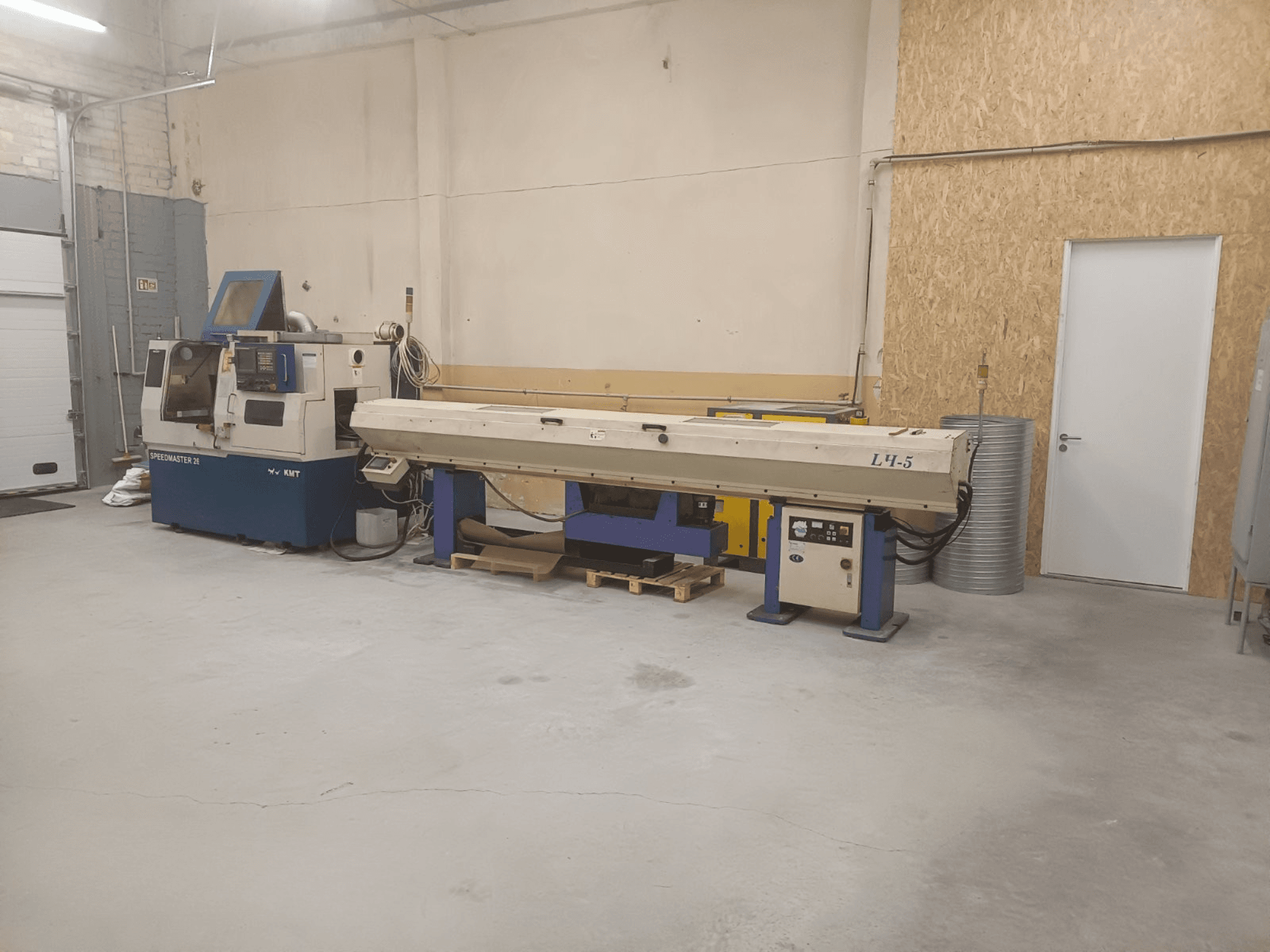 Tööstuslik töökoda, kus on KMT Speedmaster 34 masin ja L4.5, vaadatuna eestpoolt, koos nähtavate juhtimisseadmete ja masinatega.