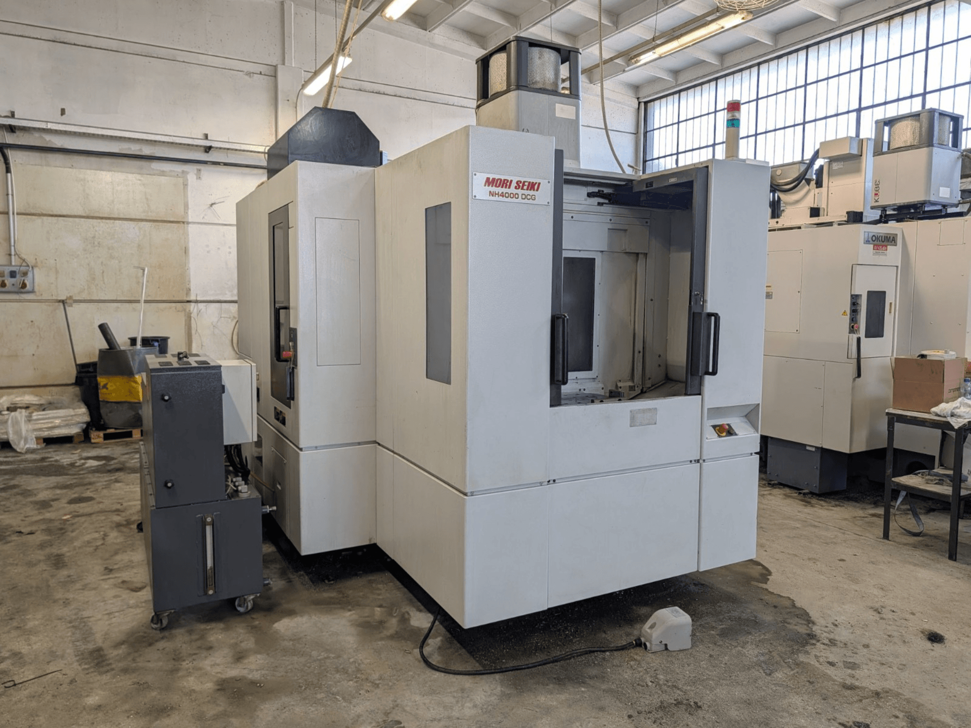 MORI SEIKI NH 4000 DCG horisontaalne töötluskeskus, esiplaanil, juhtpaneel ja tööala, hall ja valge viimistlus.