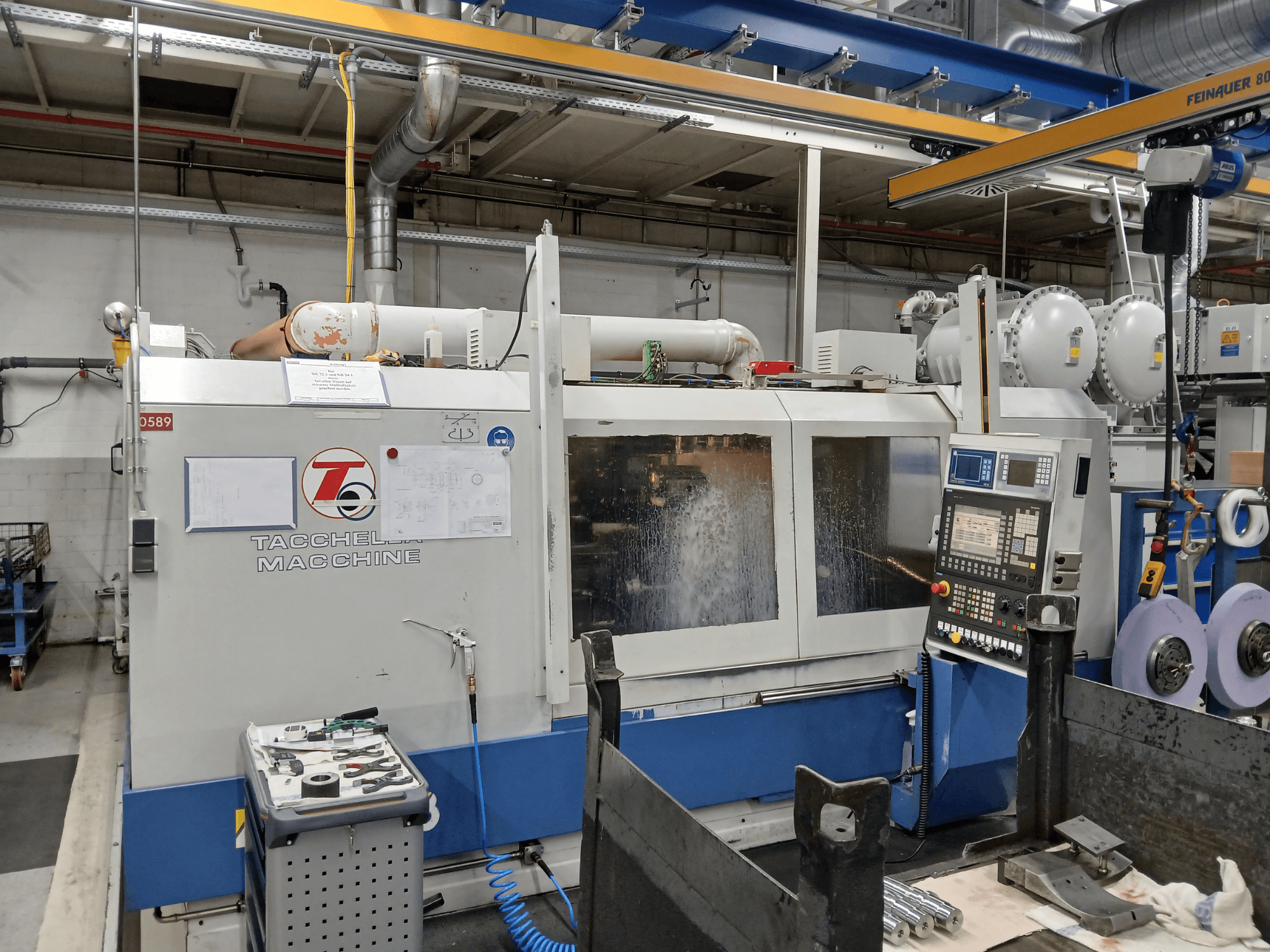 Tacchella töötluskeskus esiplaanilt, juhtpaneel ja tööriistad nähtavad. Veejahutusvedeliku pritsmed töö ajal.