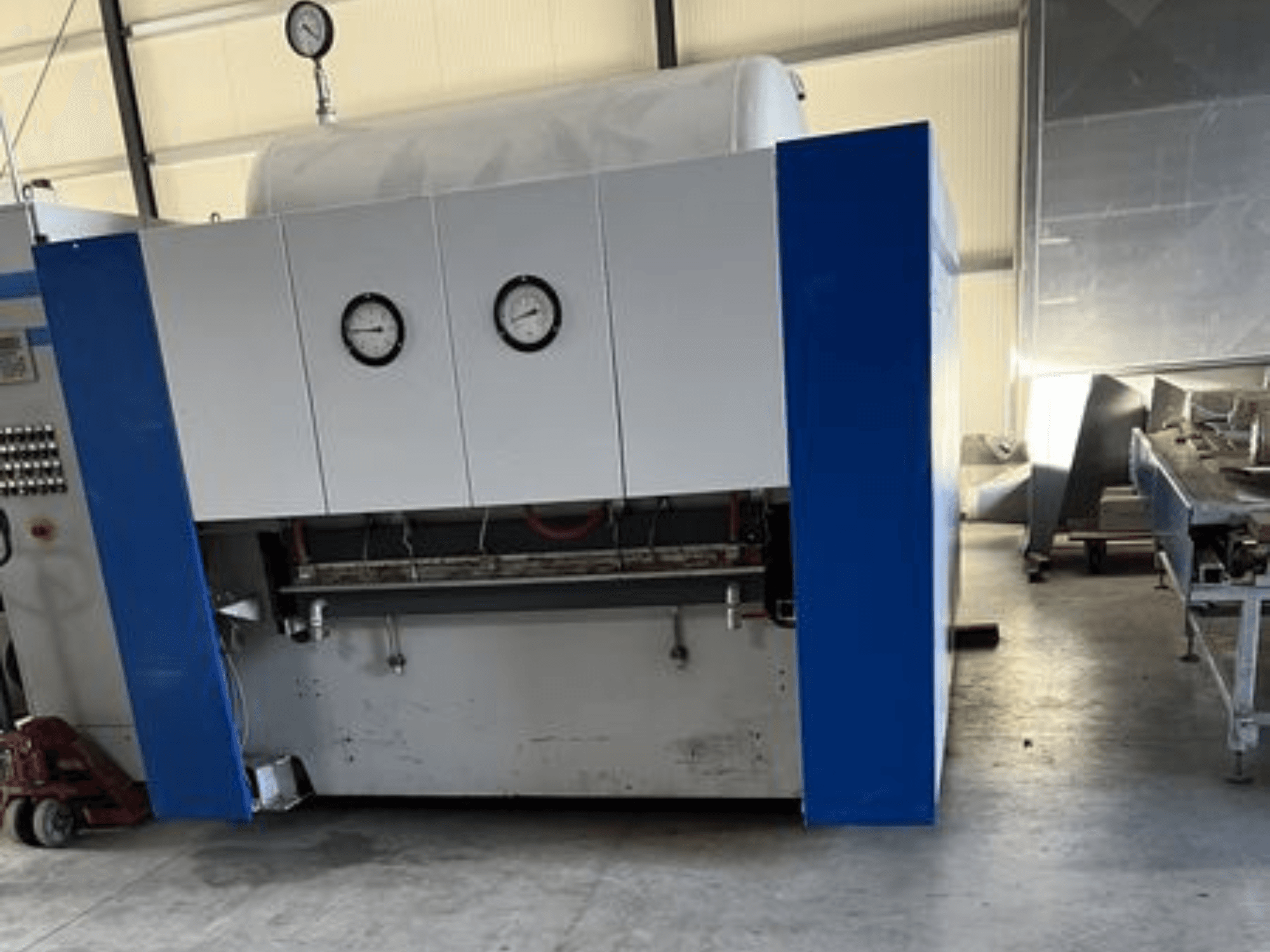 Sinine ja valge tööstuslik masin kahe rõhumõõturiga, esiplaanil, millel on juhtpaneel ja kõrvalolevad seadmed.