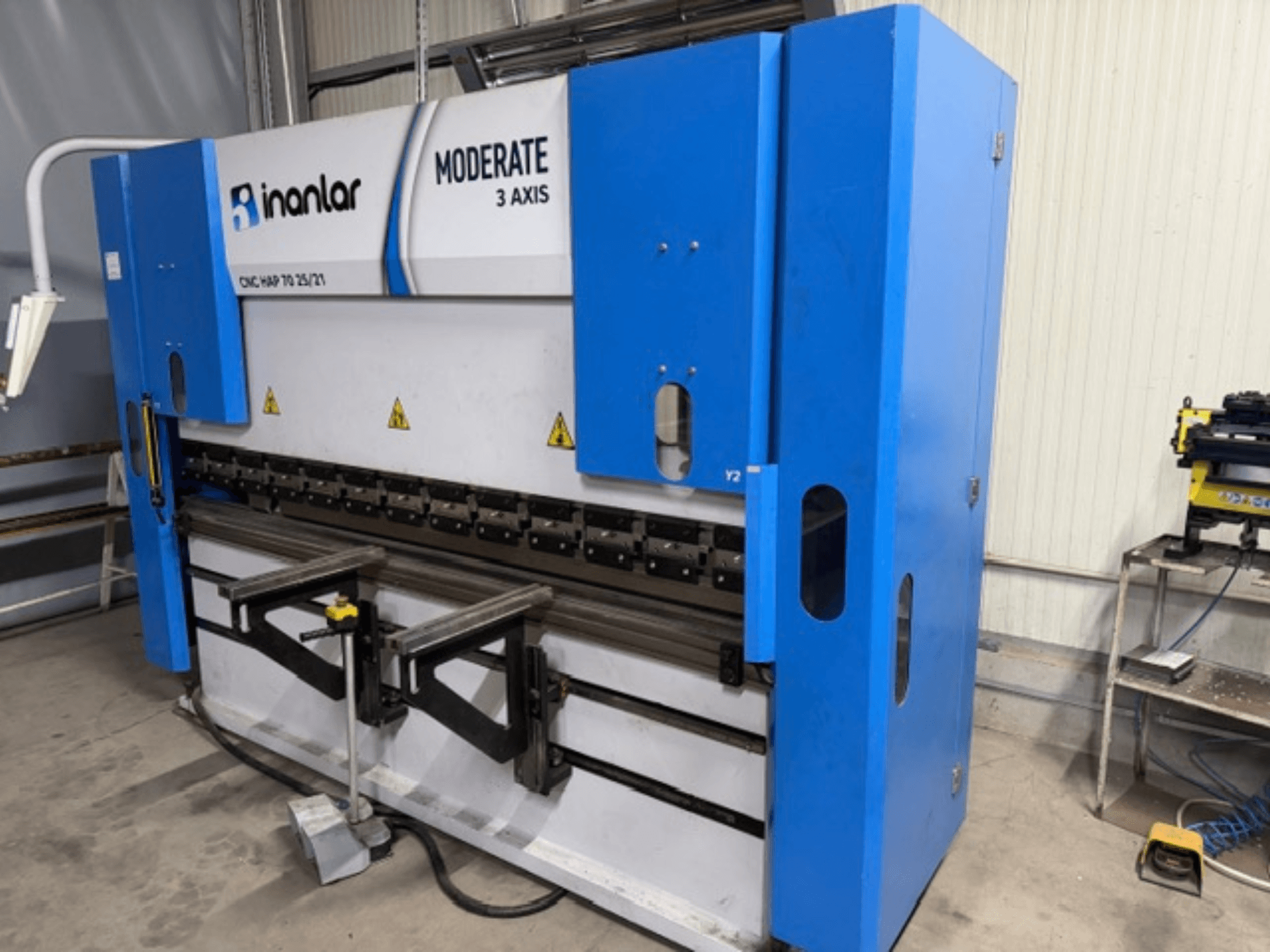 Inanlar Moderate 3-teljeline CNC-tööpink sinises toonis, esiplaanil, juhtimiskangid ja ohutussildid nähtavad korpusel.