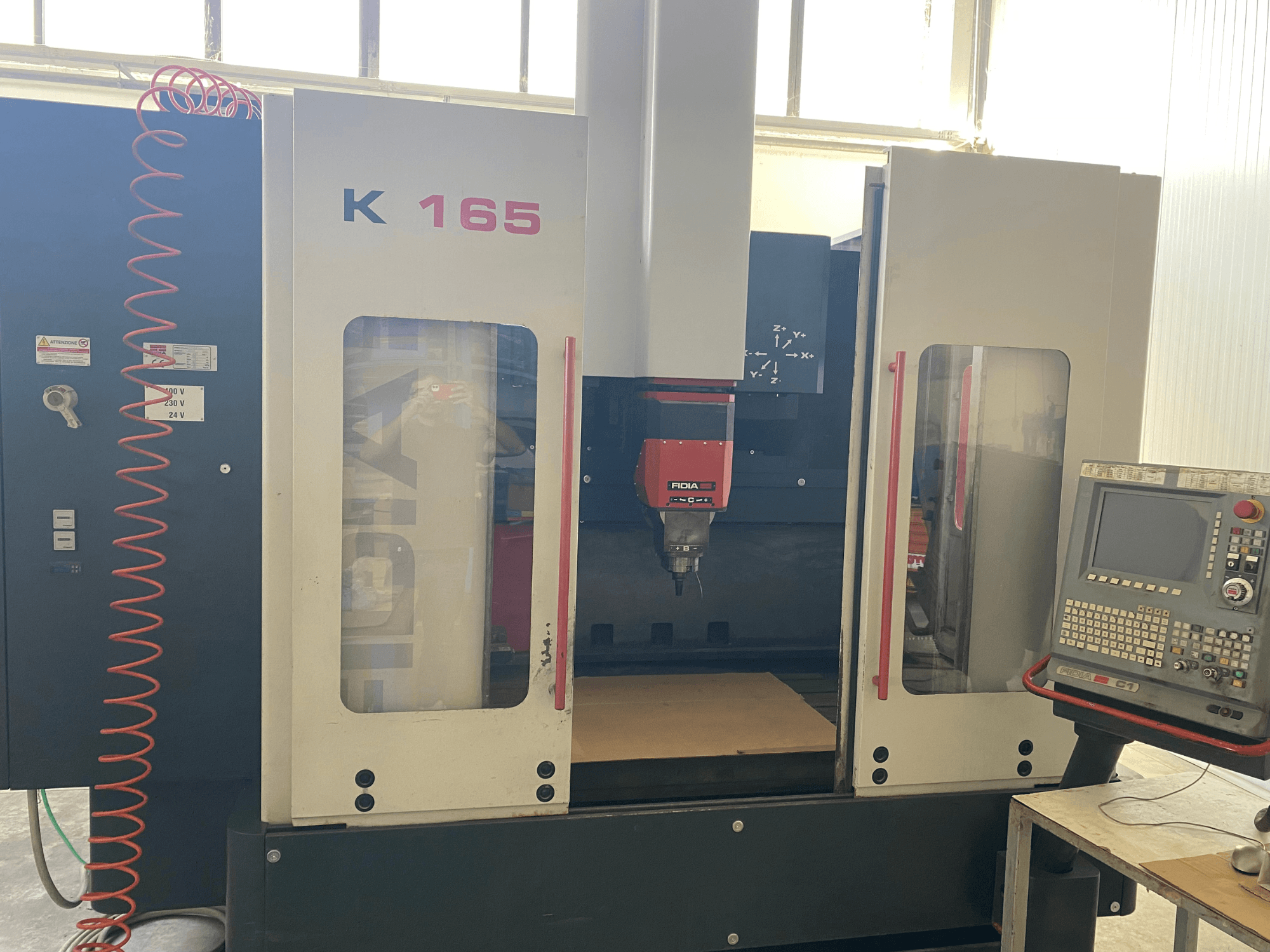 Punase spindli ja juhtpaneeliga Fidia K 165 CNC-tööpinklaadiga masin, vaadatuna eestpoolt, hästi valgustatud töökojas.