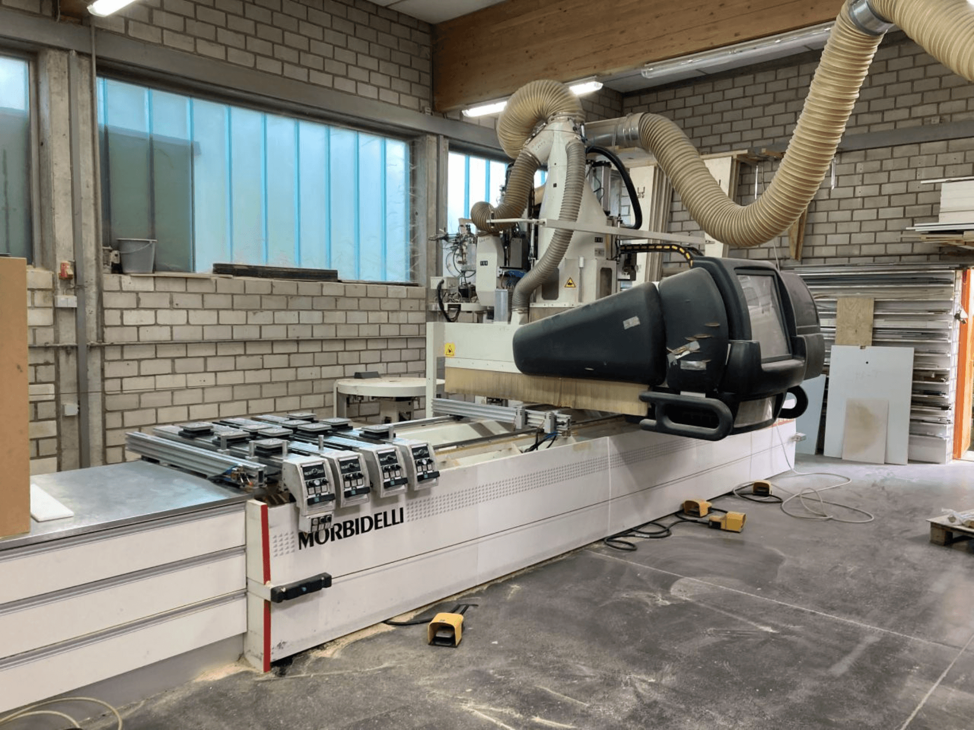 MORBIDELLI CNC-tööpink töökojas, esivaade juhtpaneeliga, tolmueemaldussüsteem ja paigutatud puidutükk.