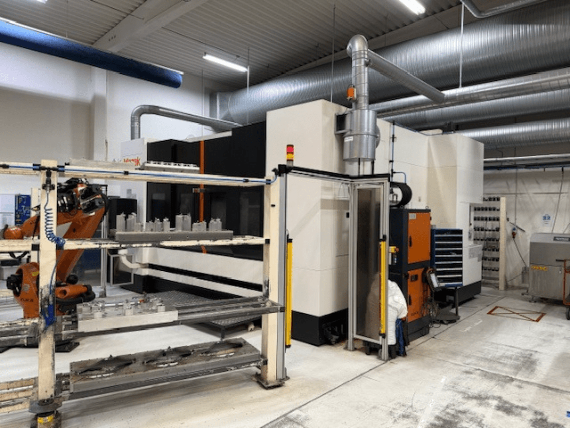 Tööstuslik CNC-tööpink koos robotkäe ja turvapiirdega, mille esiplaanil on vaade seadistusele õhulises tööruumis.