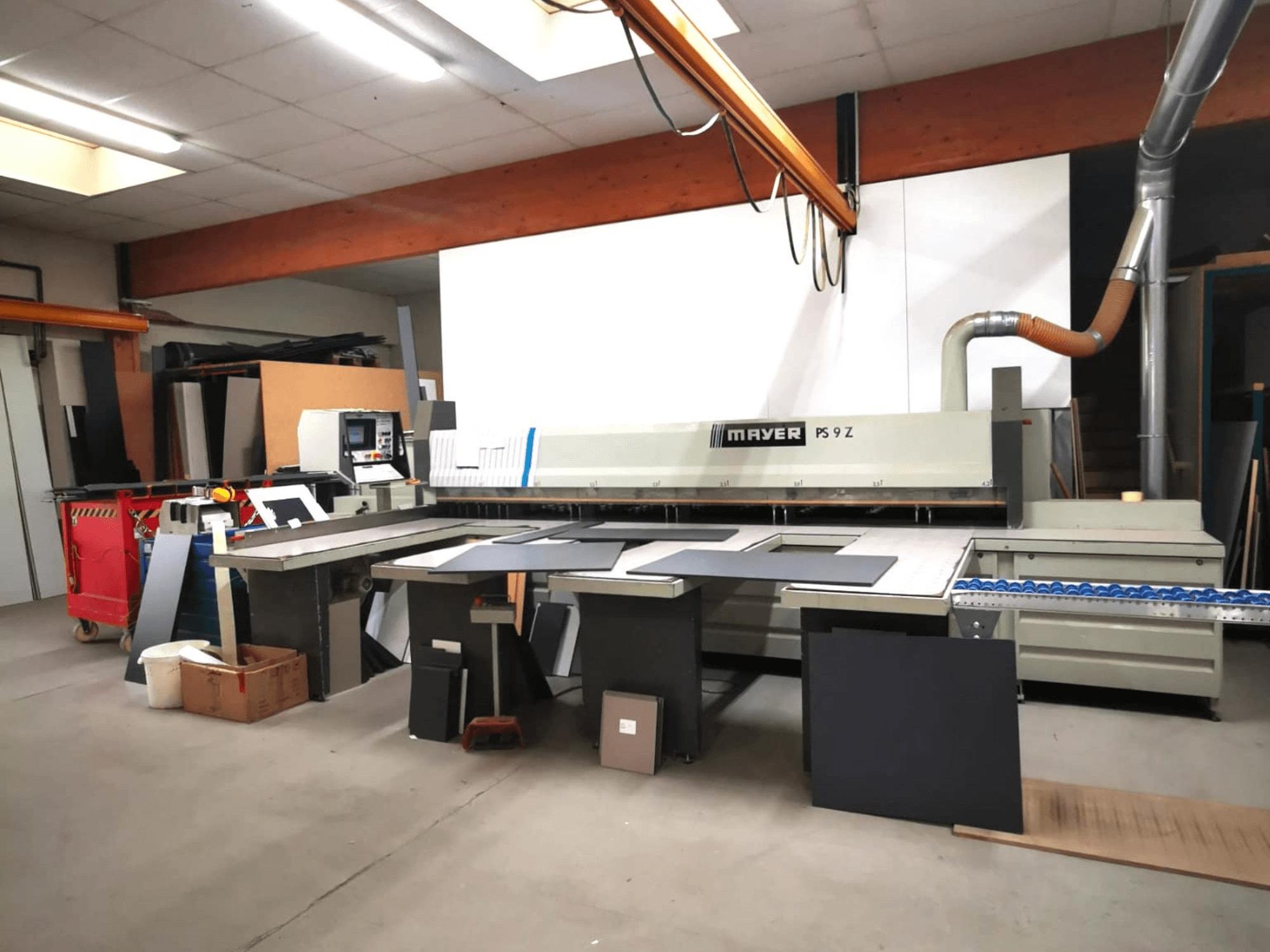 MAYER PS9 Z-lõikepink töökojas, esiplaanil, erinevad materjalid ja konveierisüsteem nähtavad.