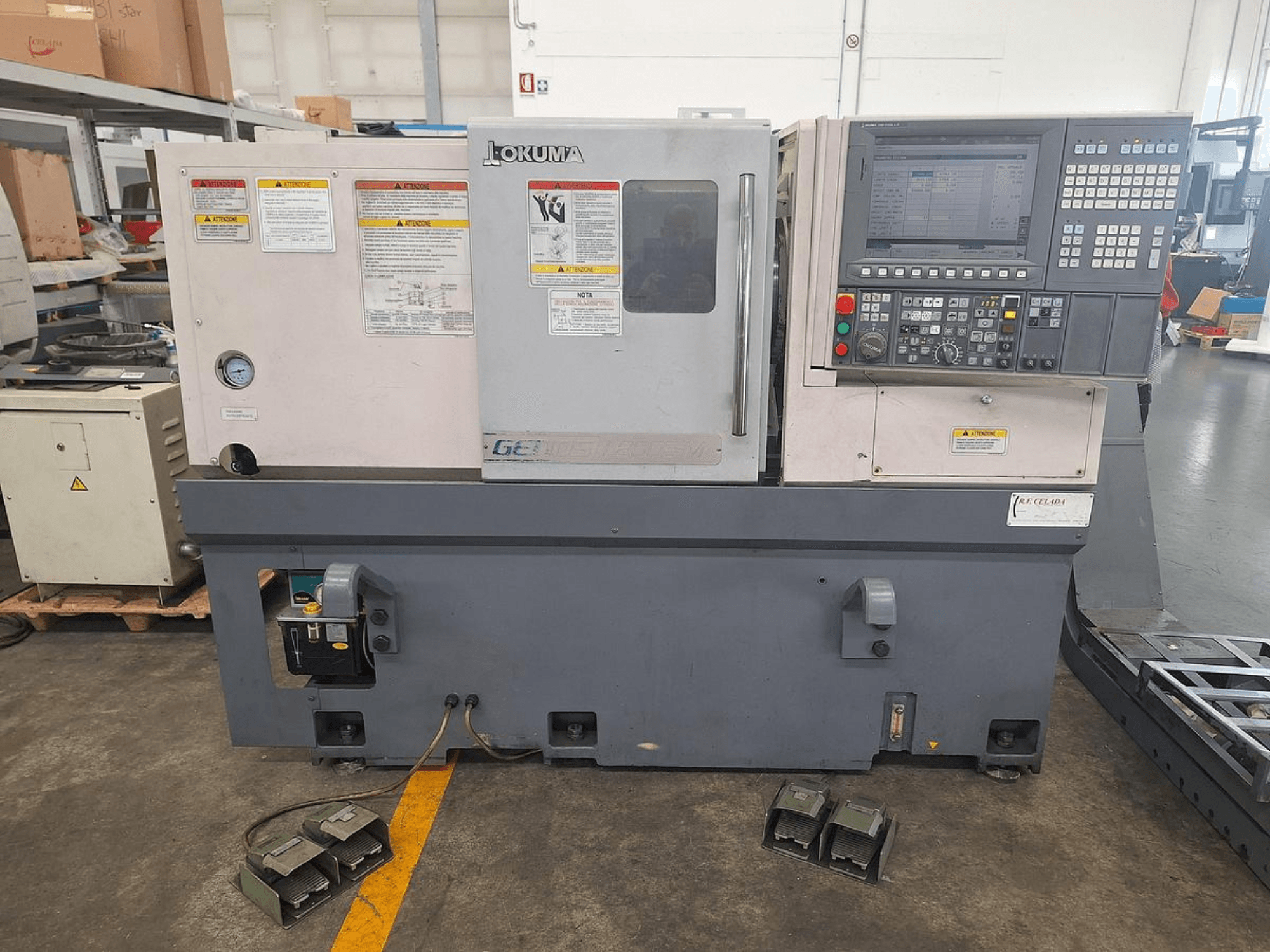 Okuma GENOS L200E-M horisontaalne treipingi külgvaates; juhtpaneel, ohutushoiatused ja jalgpedaalid.