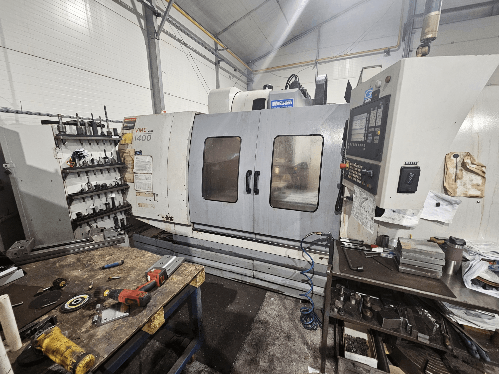 VMC 1400 CNC-freesimispink töökojas, esivaade; tööriistad ja materjalid laiali töölaual lähedal.