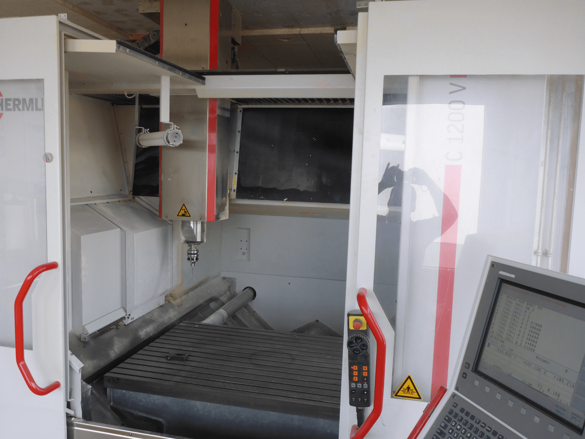 HERMLE C 1200 vertikaalne töötlemiskeskuse sisemus, millel on tööriistahoidja, juhtpaneel ja töölaud esiplaanilt.