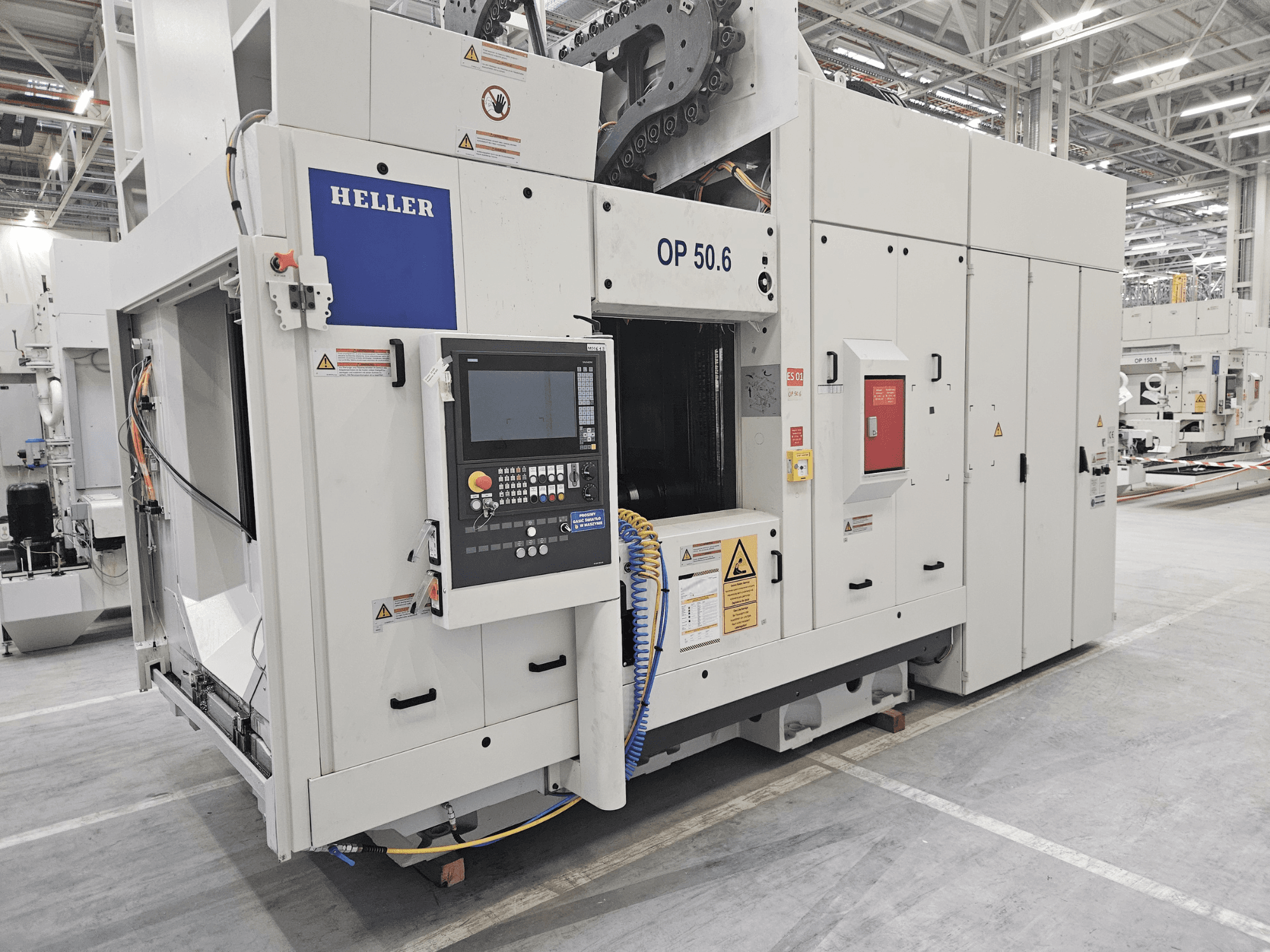 Heller OP 50.6 töötlemiskeskus, esiplaanil, juhtpaneel, hoiatussildid ja voolikud nähtavad tehases.