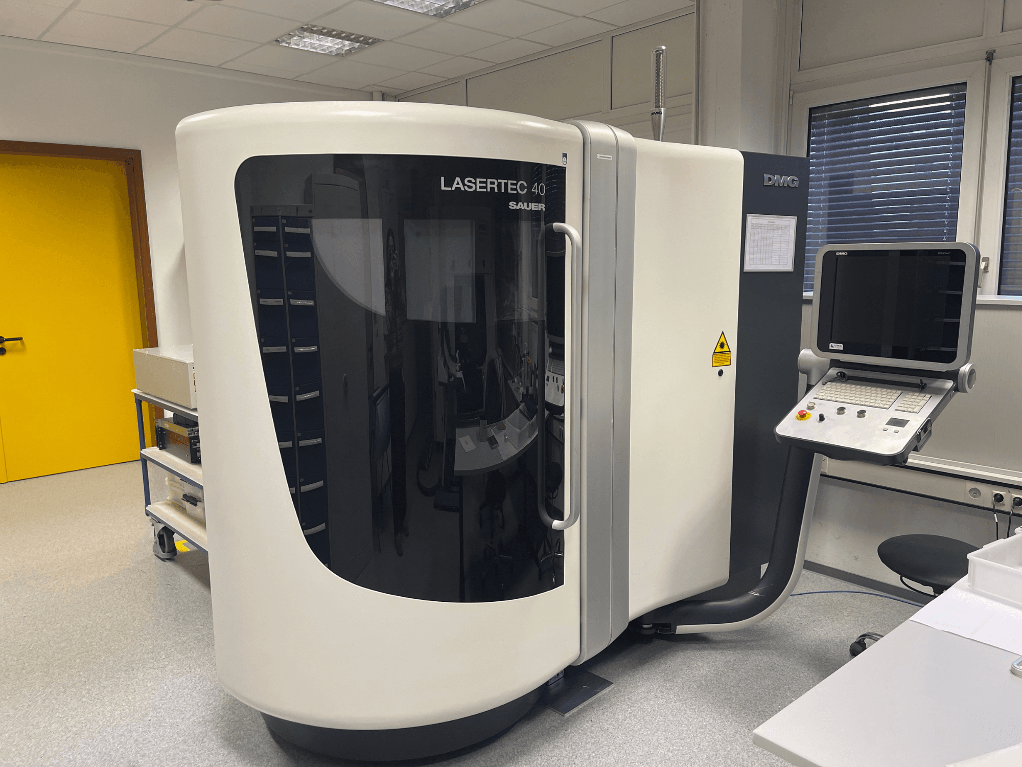 DMG MORI valge LASERTEC 40 freespink, esiplaanil, juhtpaneel ja ergonoomiline disain hästi valgustatud ruumis.