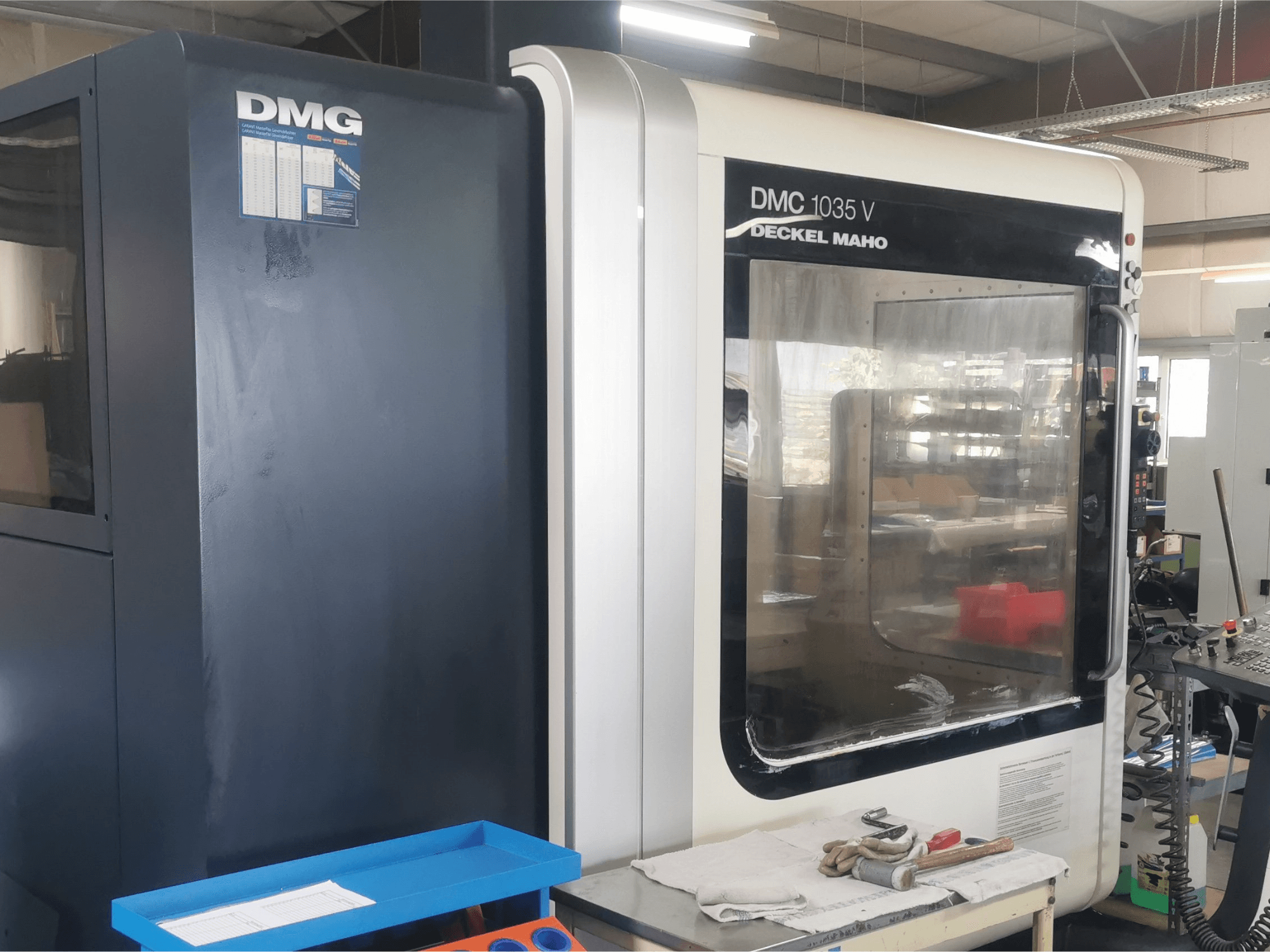 DMG DMC 1035 V freespink töökojas, esivaade sinise tööriistakasti ja kinnastega pinnal.
