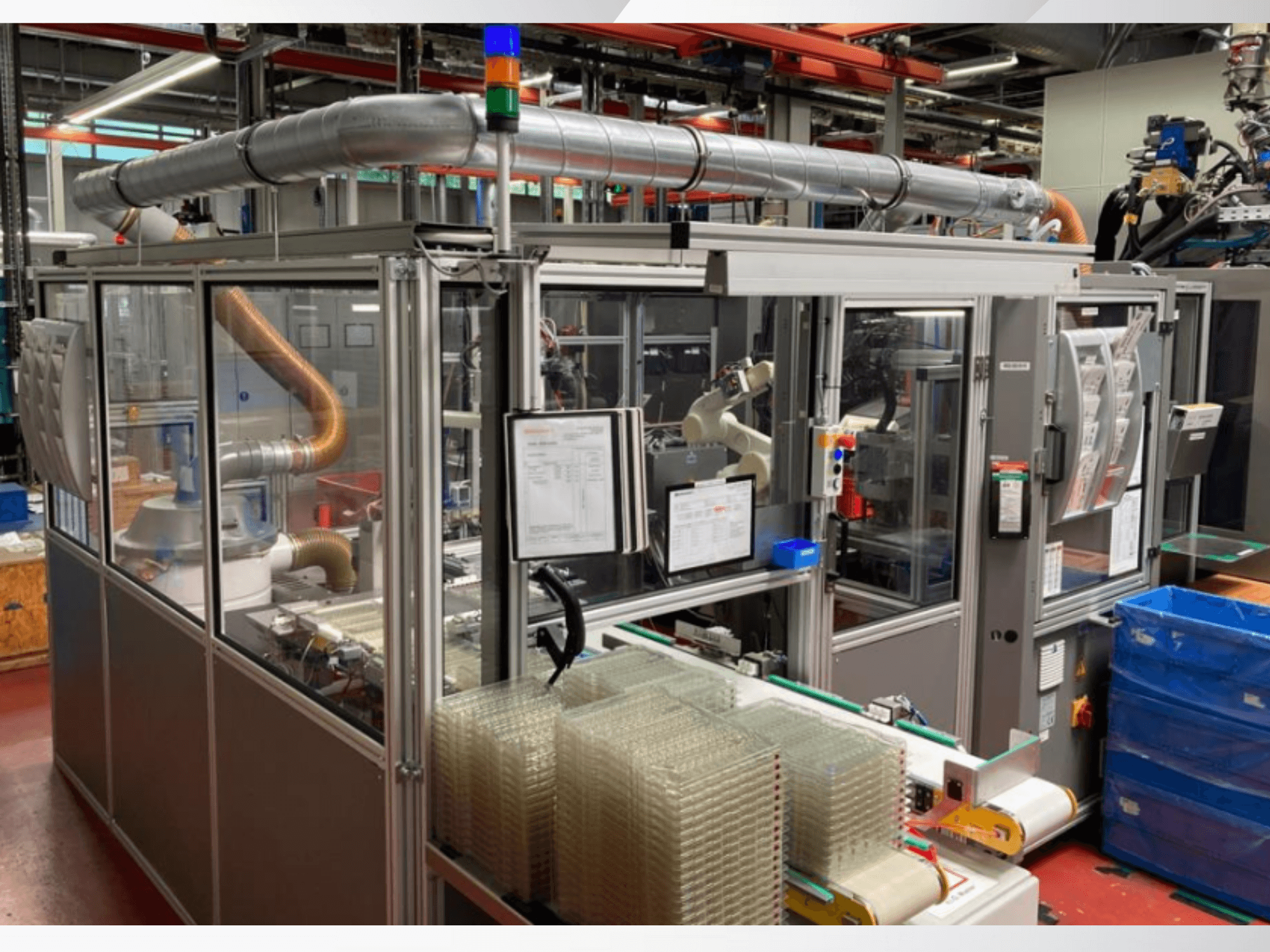 Automaatne komplekteerimismasin robotkäe, läbipaistvate külgpaneelide ja läbipaistvate esemete virnastatud konteineritega, esiplaanil.