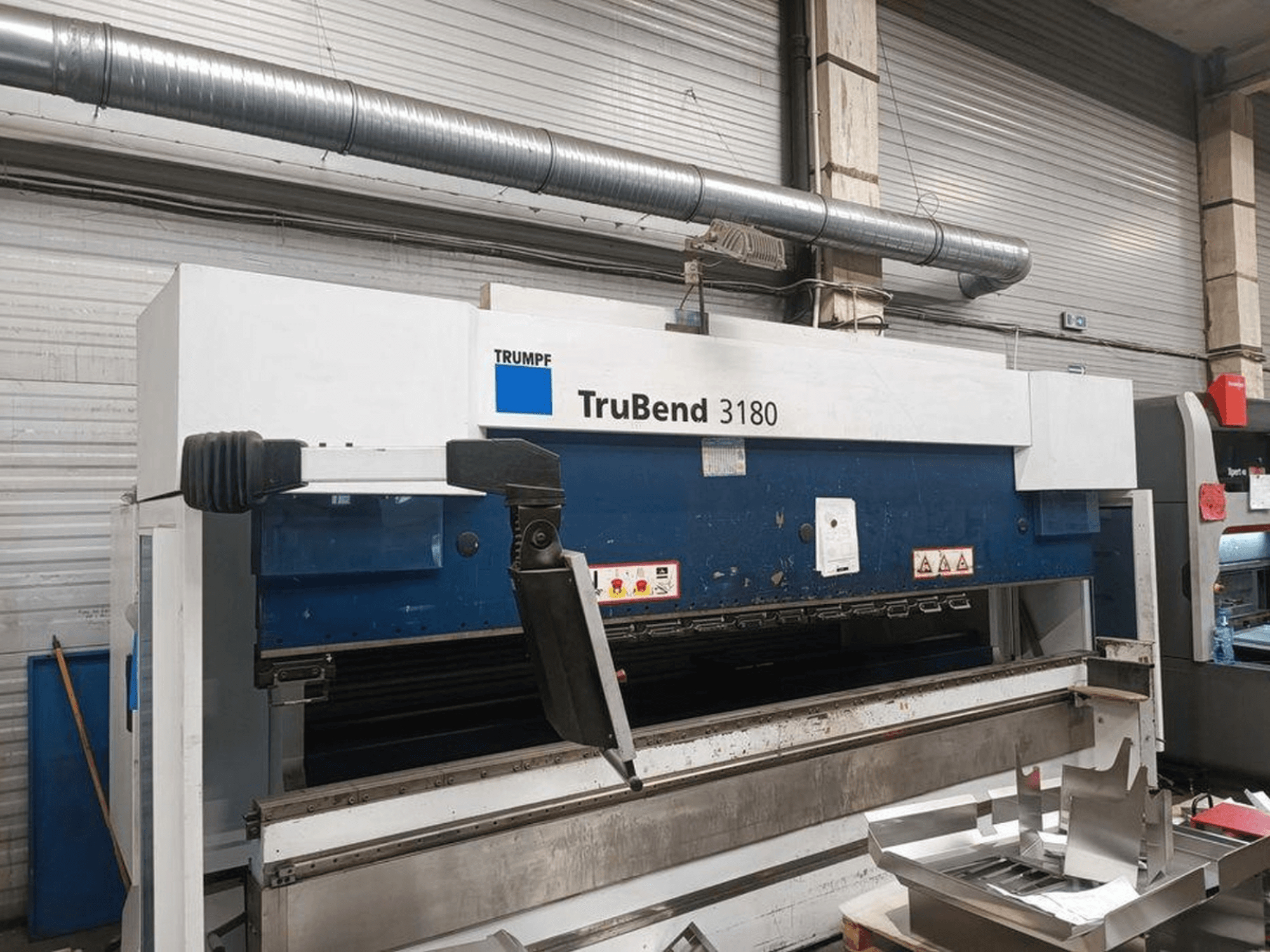Trumpf TruBend 3180 painutuspink töökojas, külgvaates on näha juhtpaneel ja metallitükid laual.