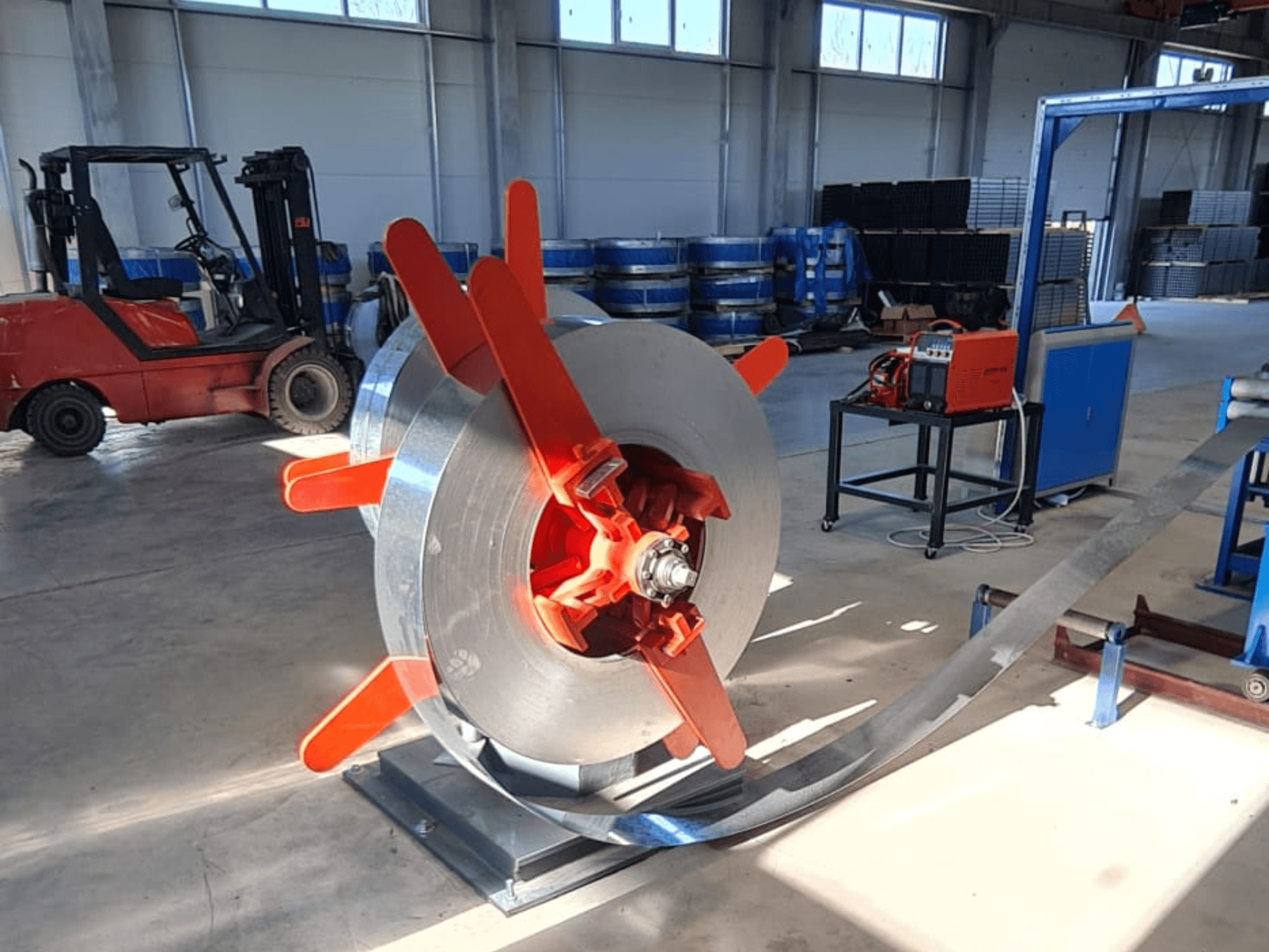 Punaste käepidemetega metallspiraal stendil, nurga alt vaadatuna. Tööstuslik taust koos masinate ja kahveltõstukiga.