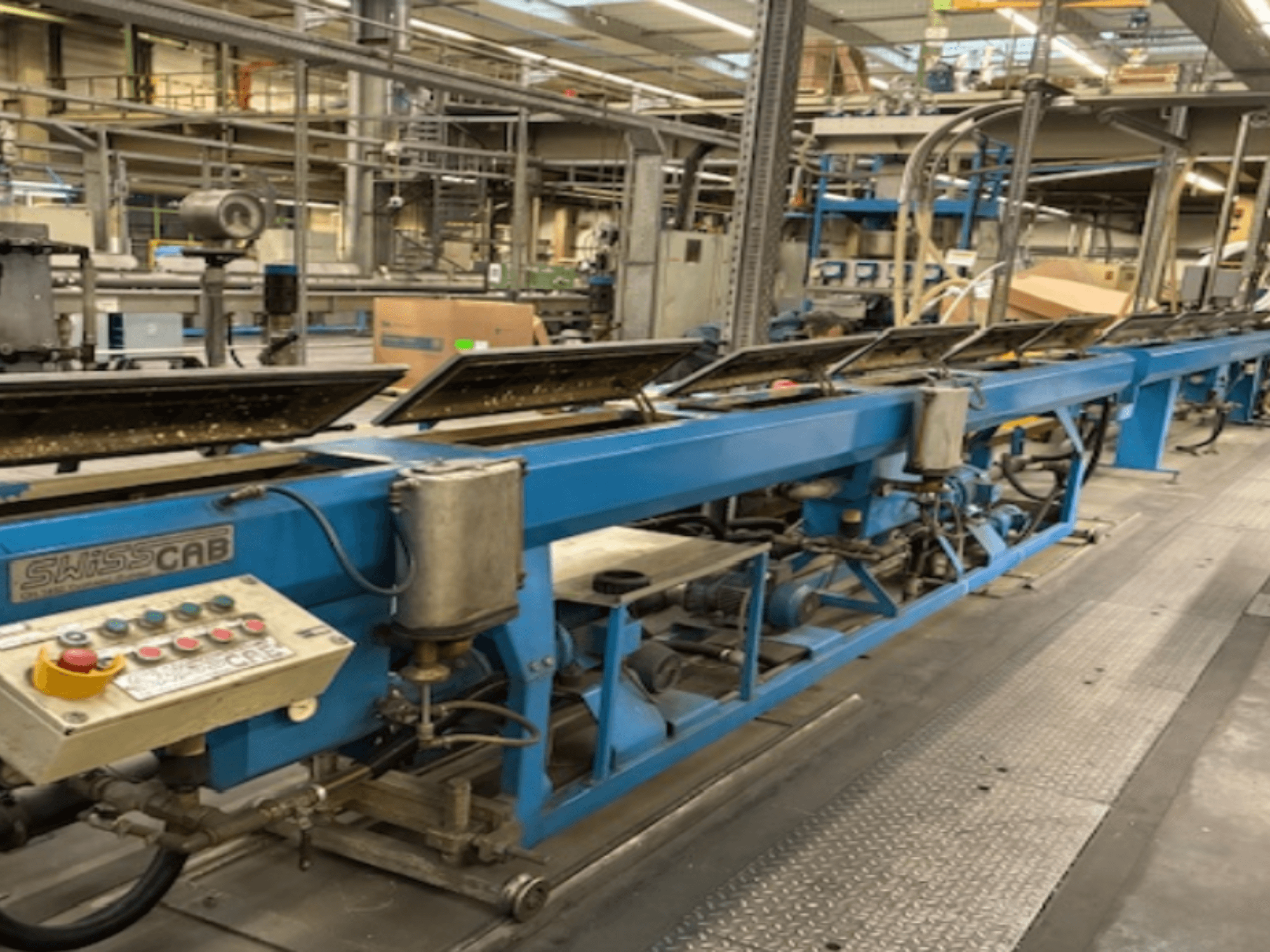 Sinine SwissCab tööstusmasin tehases, millel on kasutamisnupud ja konveierisüsteem, külgvaade.