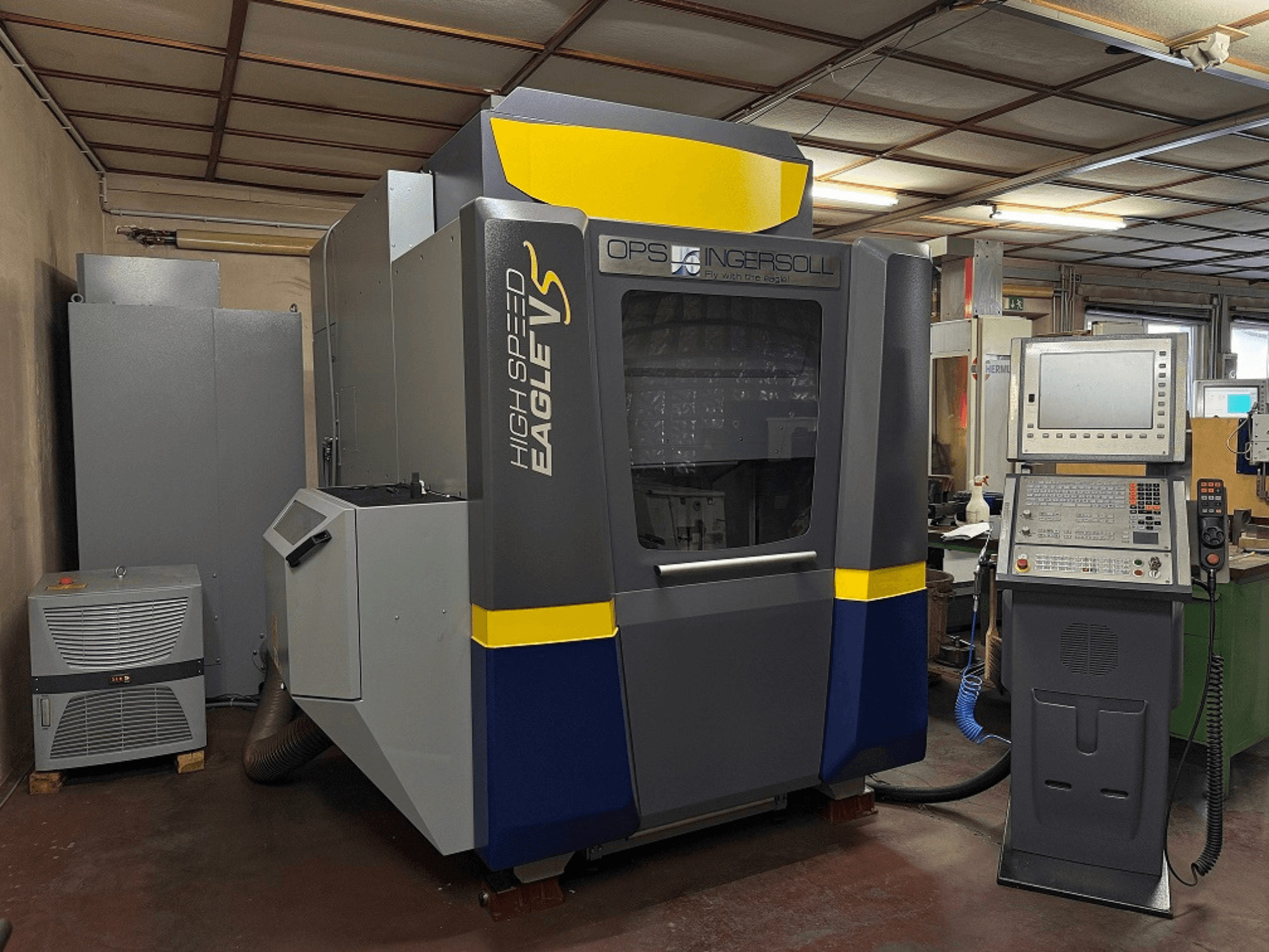 OPS Ingersoll'i kiire Eagle V masin, külgvaade, koos juhtpaneeli ja kõrvalolevate seadmetega tööstuslikus keskkonnas.