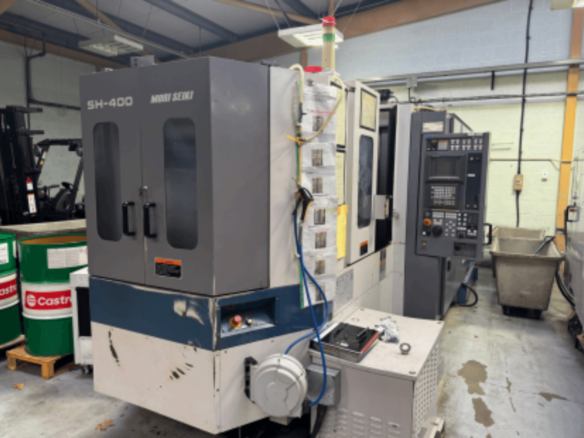 Moni Seiki SH-400 CNC masin, külgvaade, kus on näidatud juhtpaneel, uksed ja ümbritsev tööstuskeskkond.