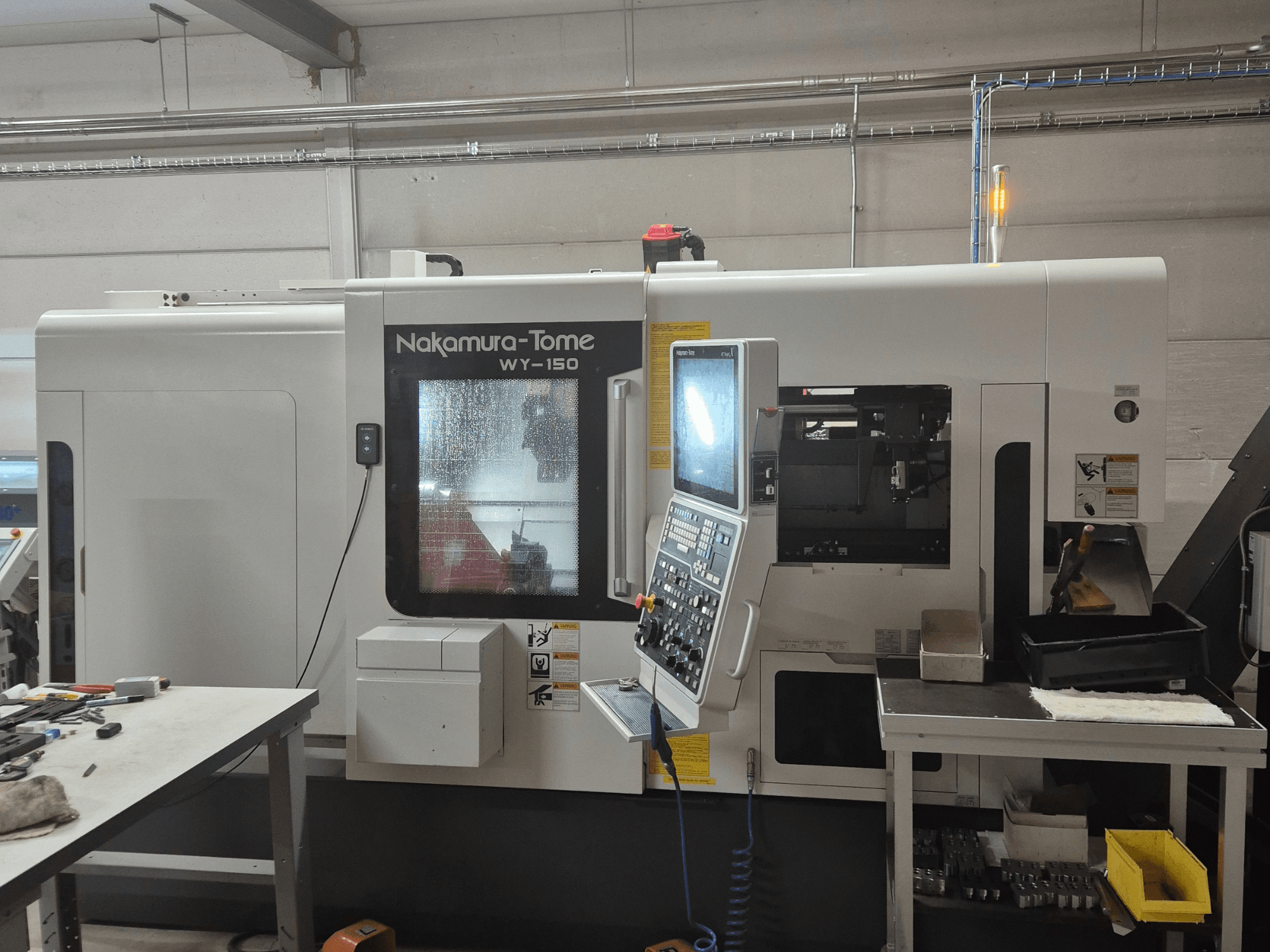 Nakamura-Tome WY-150 CNC-teeninduspingi külgvaade, millel on juhtpaneel, läbipaistev aken ja nähtav tööala.