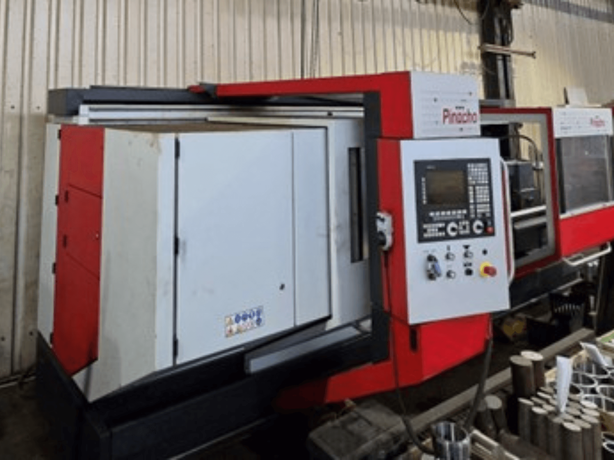 Pinacho CNC-tööpink punavalge, külgvaade, juhtpaneel ja materjalid põrandal, näitab tööseadistust.