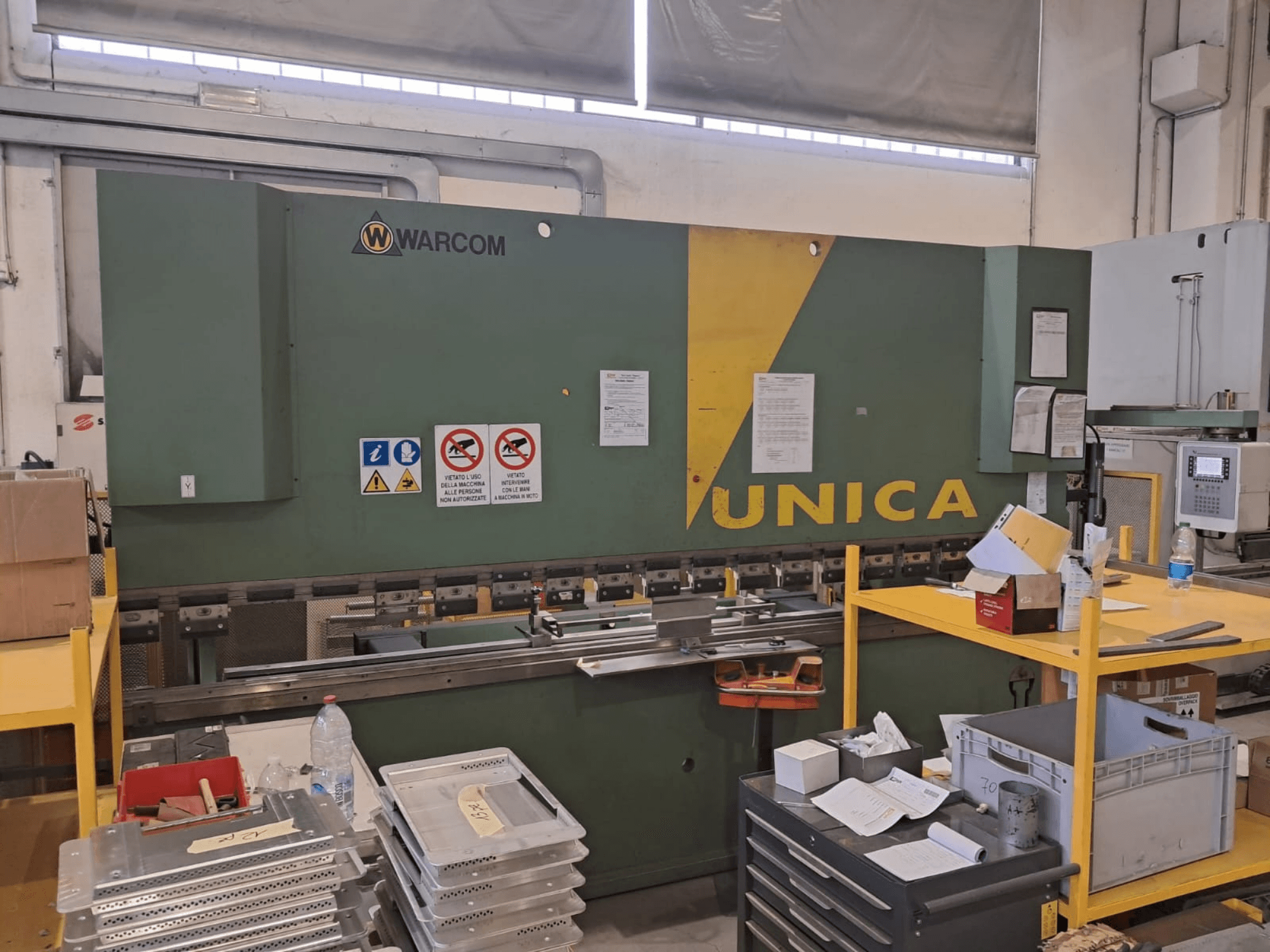 Hüdrauliline press Warcom UNICA 100-40, vaade eest, roheline korpus kollaste detailidega, ohutusmärgid on nähtavad, tööriistad ja materjalid laual.