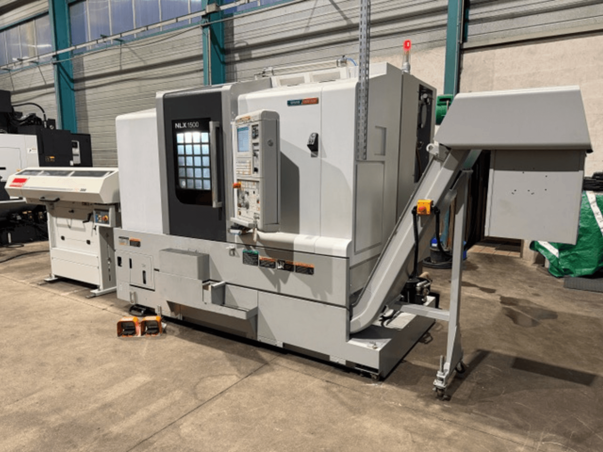 NLK 1500 CNC masin, esiplaanil, juhtpaneel ja tarvikute punker küljel, betoonpõrandal.