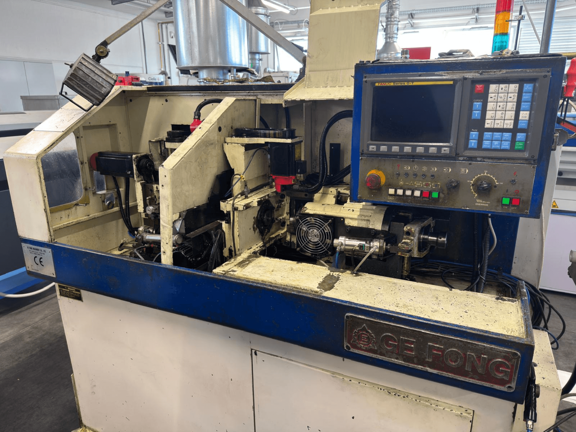 GE FONG tööstusmasin esiplaanil, millel on näha sisemised komponendid, juhtpaneel ja töötavaid osi.
