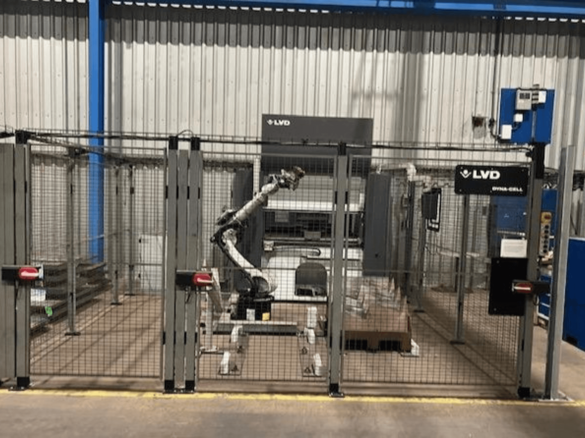 LVD Dyna-Cell robootika tööjaam aiaga ümbritsetud korpuses, esivaade, robotkäe ja juhtpaneeliga.