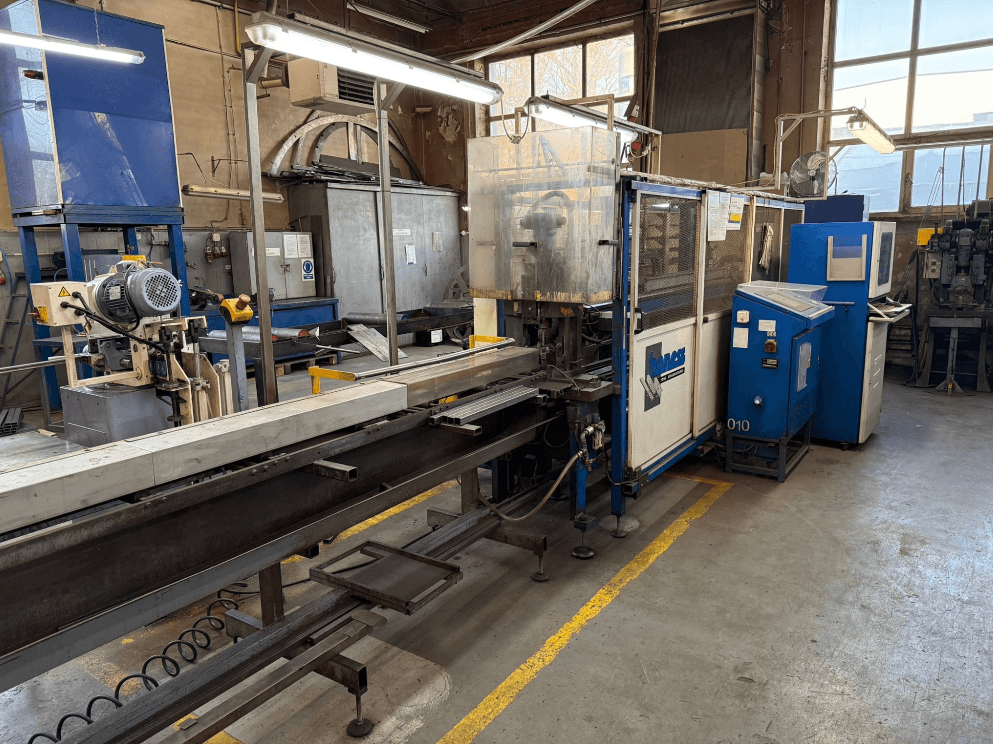 Tööstuslik töökoda sinise Hawease masinaga, külgvaates on näha konveier ja seadmed suures, hästi valgustatud ruumis.