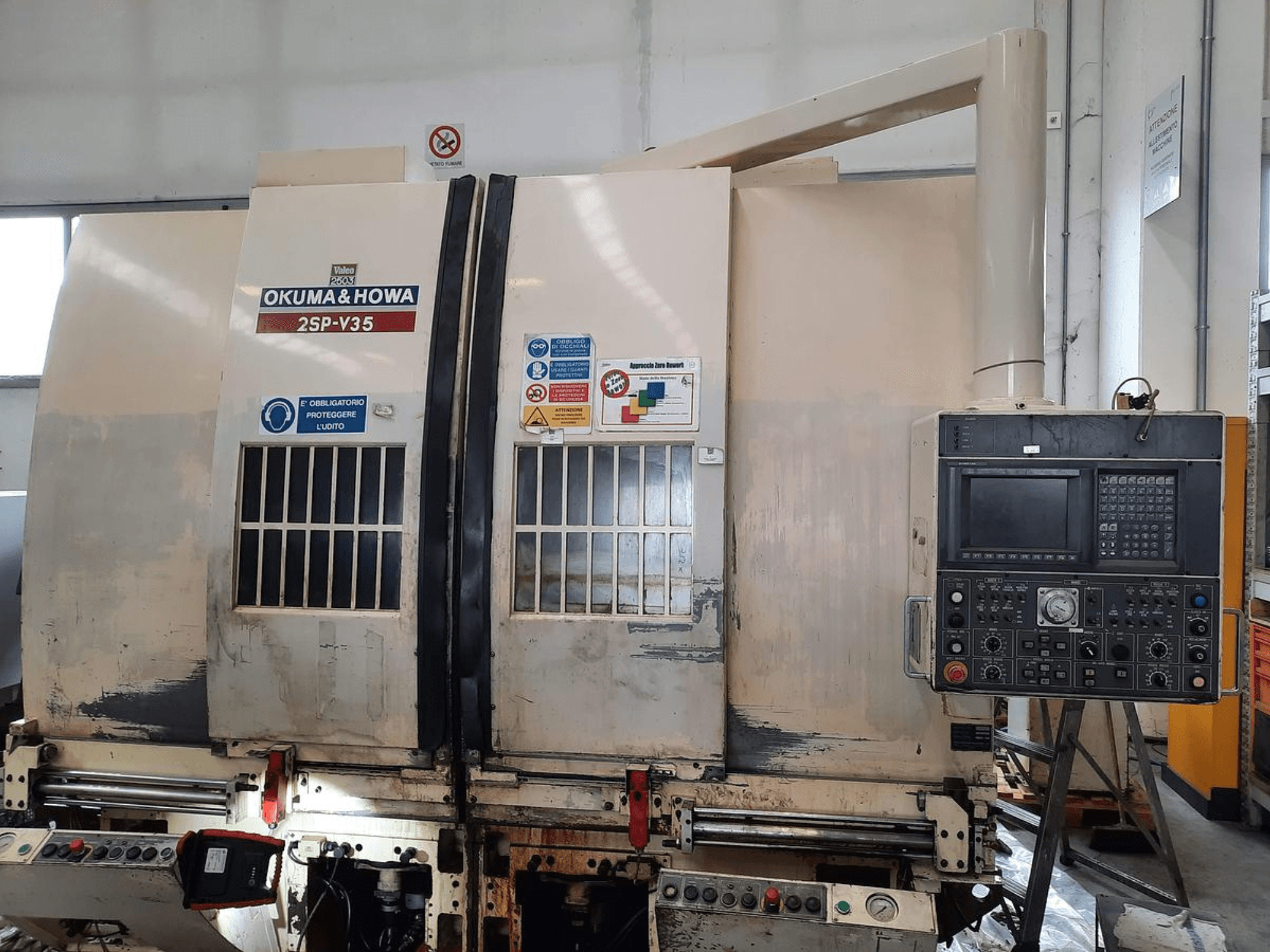 OKUMA & HOWA 2SP-V35 CNC-tööpink ees, millel on juhtpaneel erinevate nuppude ja ohutussiltidega.