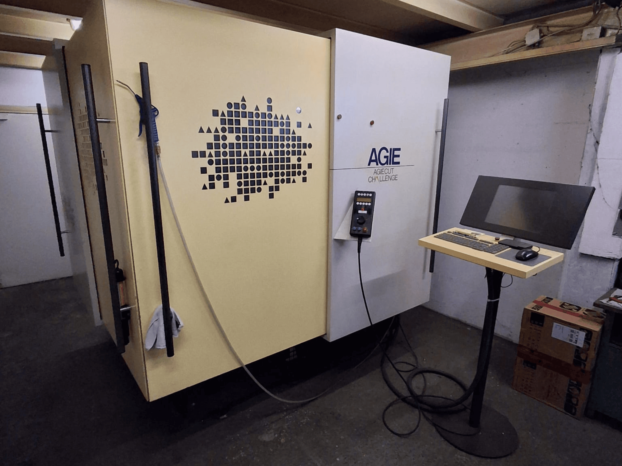 Töökojas asuv AGIE Agiecut Challenge kahejuhtmeline elektrosüütega töötlemismasin, millel on alusel asuv juhtpaneel ja monitor, vaade eest.