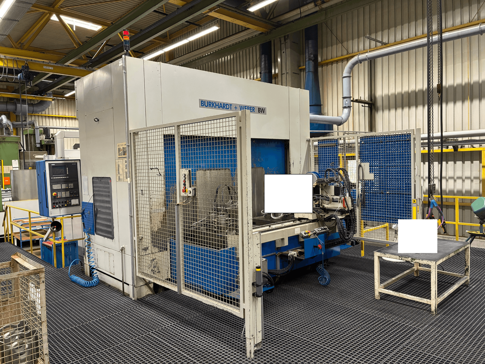 Burkhardt + Weber BW töötluskeskus, esiplaanil, juhtpaneel ja turvakapp, asub tööstuslikus keskkonnas.