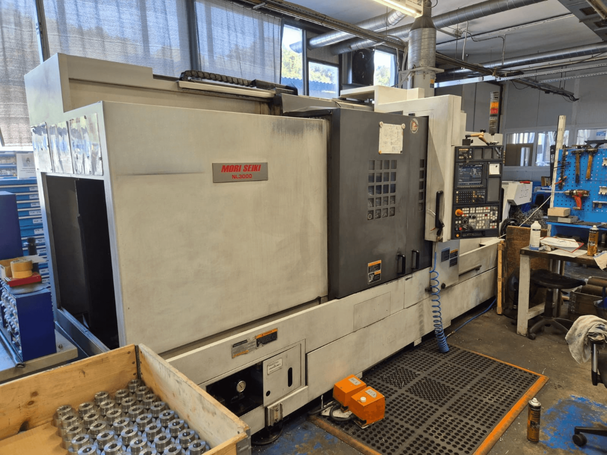 Mori Seiki NL3000 CNC-tööpinklaas töökojas, külgvaates on näha juhtpaneel, tööriistad ja metallosad puukastis.