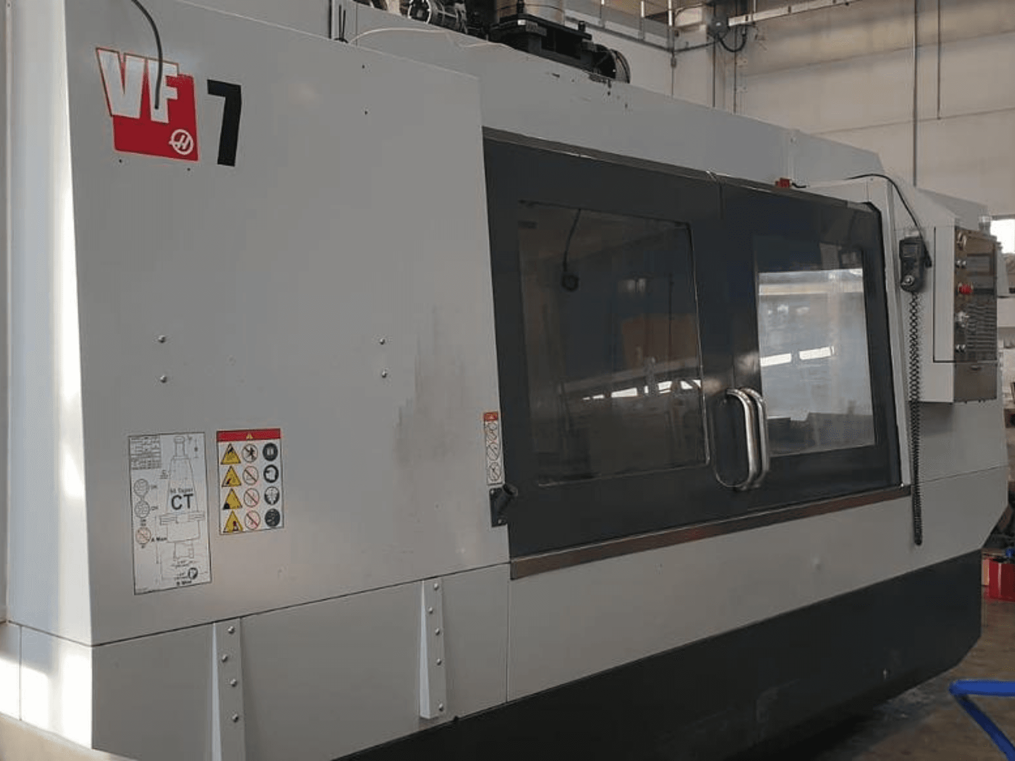 Haas VF-7 CNC-tööpingi külgvaade, millel on metallhall viimistlus, juhtpaneel ja ohutussildid.