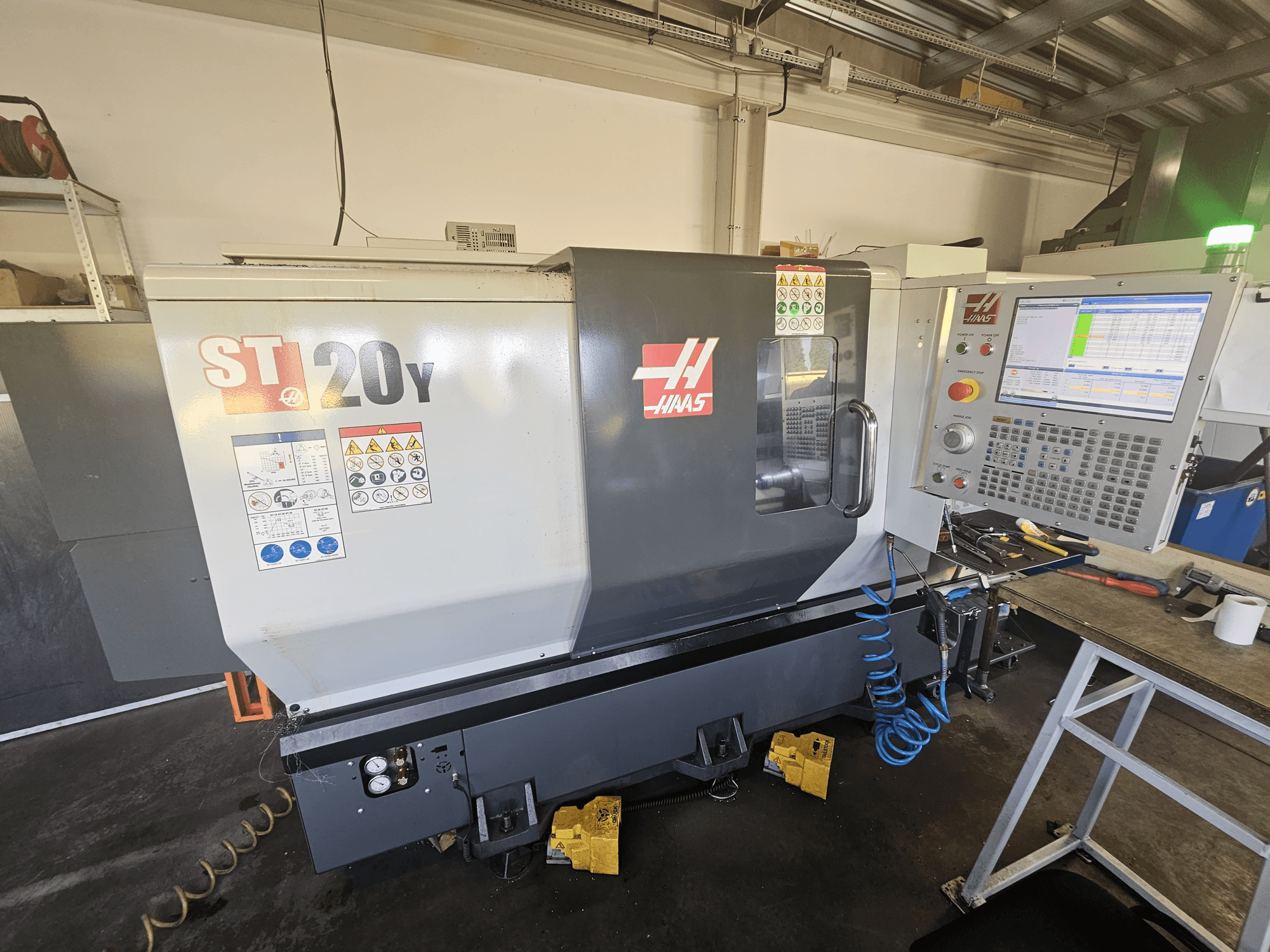 Haas ST-20Y CNC-tööpink eesvaates koos juhtpaneeliga; sisaldab ohutussilte ja õhuvooliku üksikasju küljel.