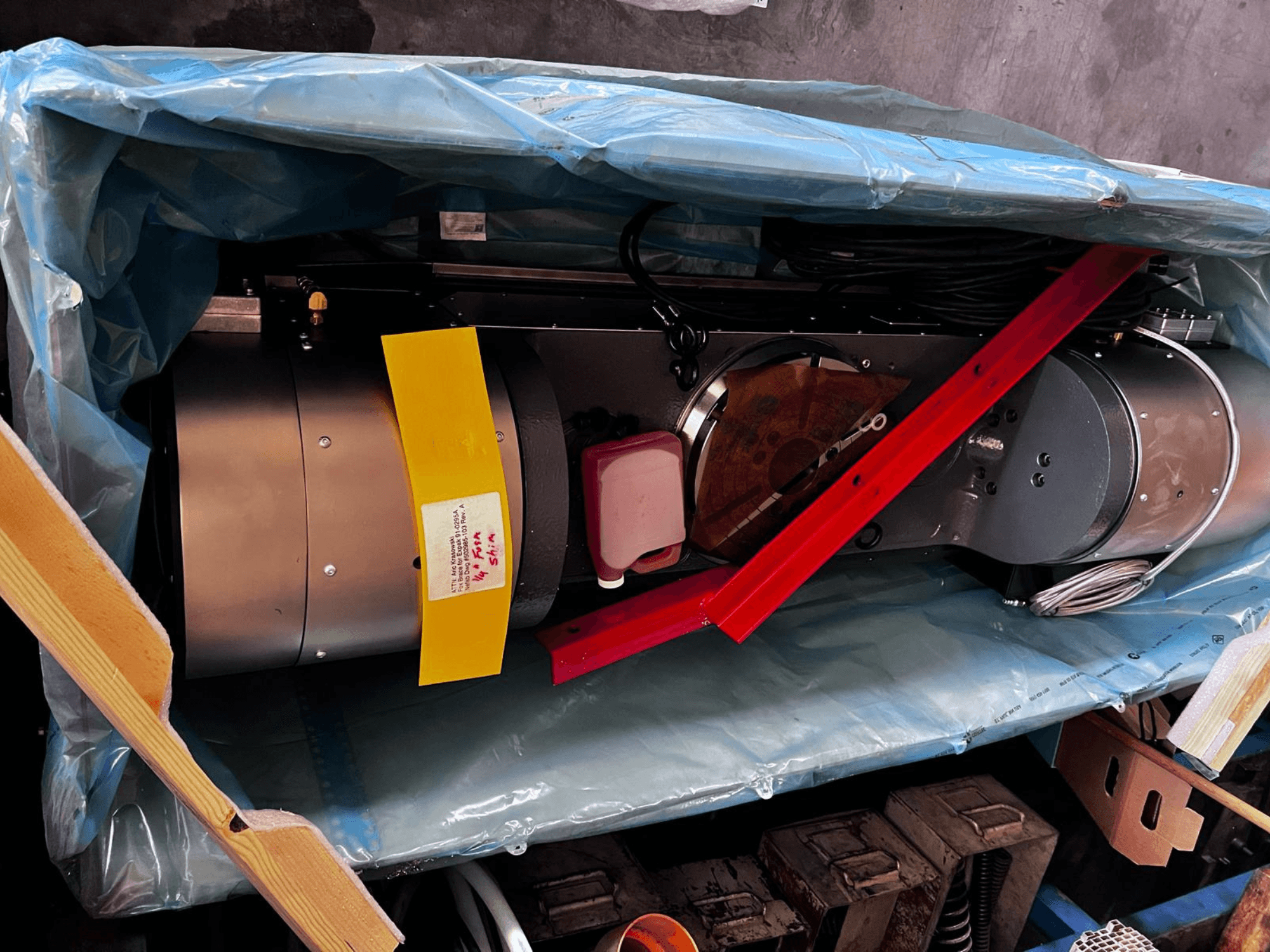 Pakendis osaliselt nähtav mootoriseade, millel on hõbedane välispind, värvilised näidikud ja punane tugiraud.