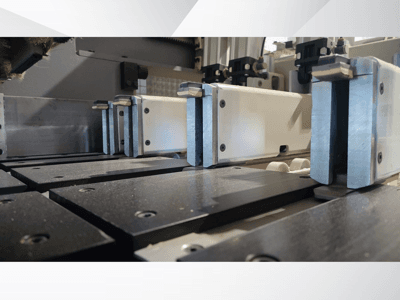 Lähivaade metallist lõugadega täppismasina kinnitusmehhanismile, millel on mustad tööpinnad ja nähtavad juhtrööpad.