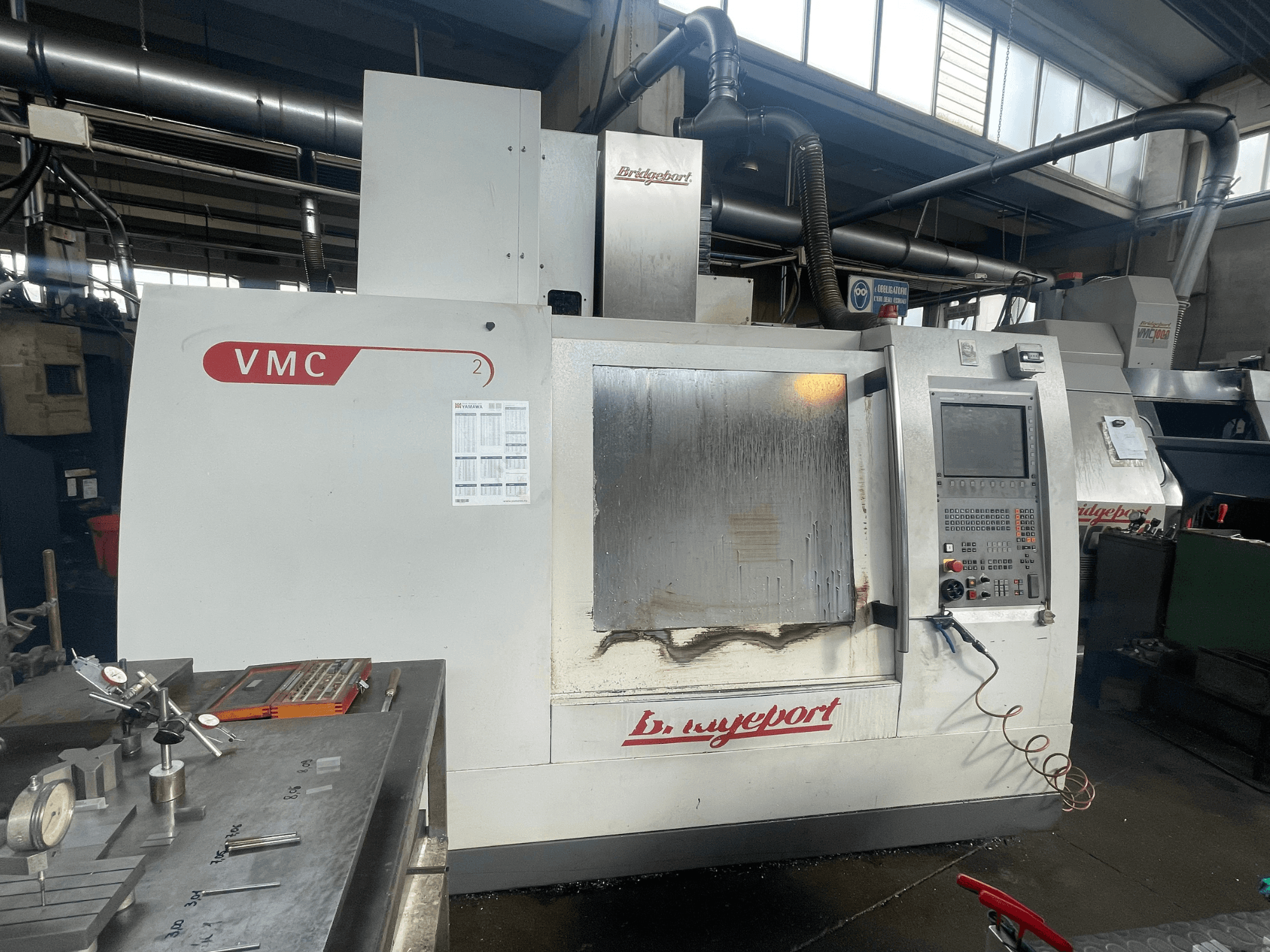 Töökojas asuv Bridgeport VCM 800-30 vertikaalne töötlemiskeskus, millel on juhtpaneel ja tööriistalaud. Eesvaade, millel on näha üksikasjad.