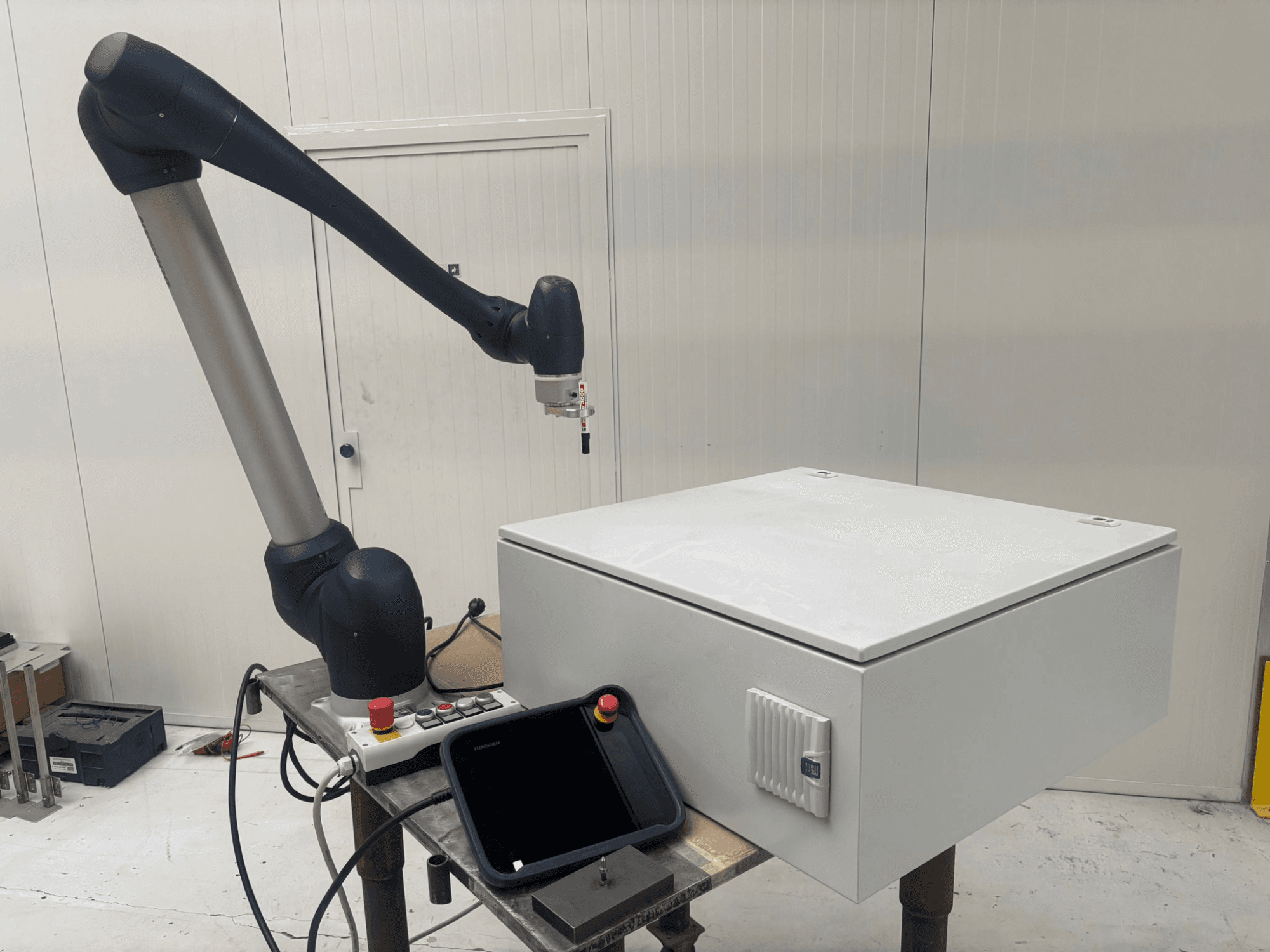 Koostöörobot DOOSAN M0617 külgvaates, robotkäsi välja sirutatud juhtimisliidese ja laual oleva valge kasti kohal.