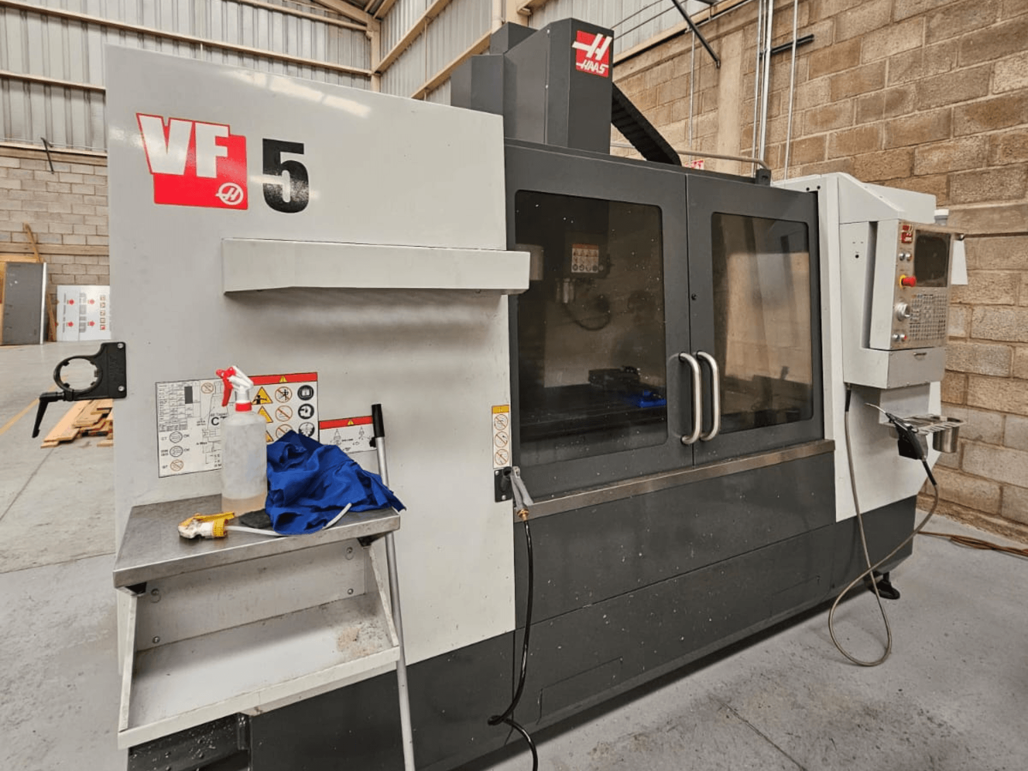 Haas VF-5 CNC-freesping eesvaates, millel on juhtpaneel, jahutusvedeliku pudel, sinine lapp ja ohutusjuhendid.