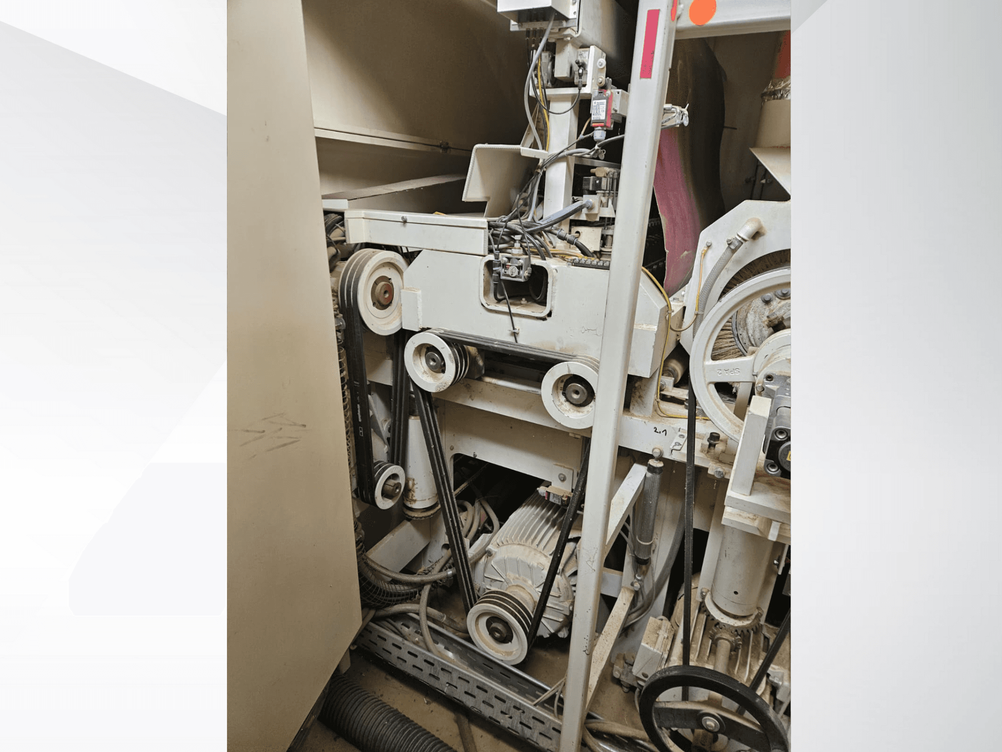 Tööstusmasina sisemus rihmade ja rihmaratastega, millel on mootor ja juhtmestik, küljelt vaadatuna.