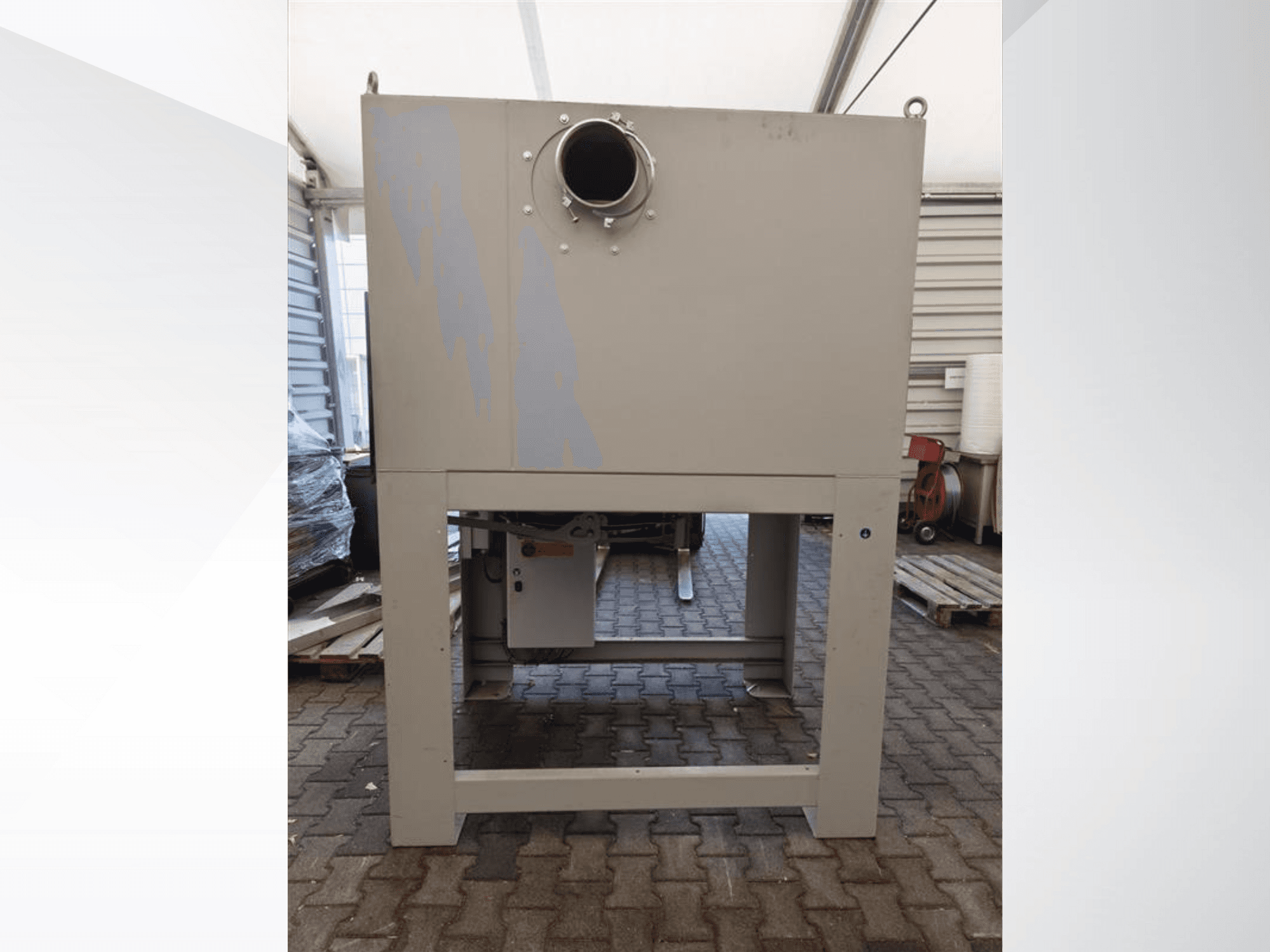 Hall tööstuslik tolmukoguja esiplaanil, millel on suur ümmargune ava ja mis on paigaldatud tugevale alusele.