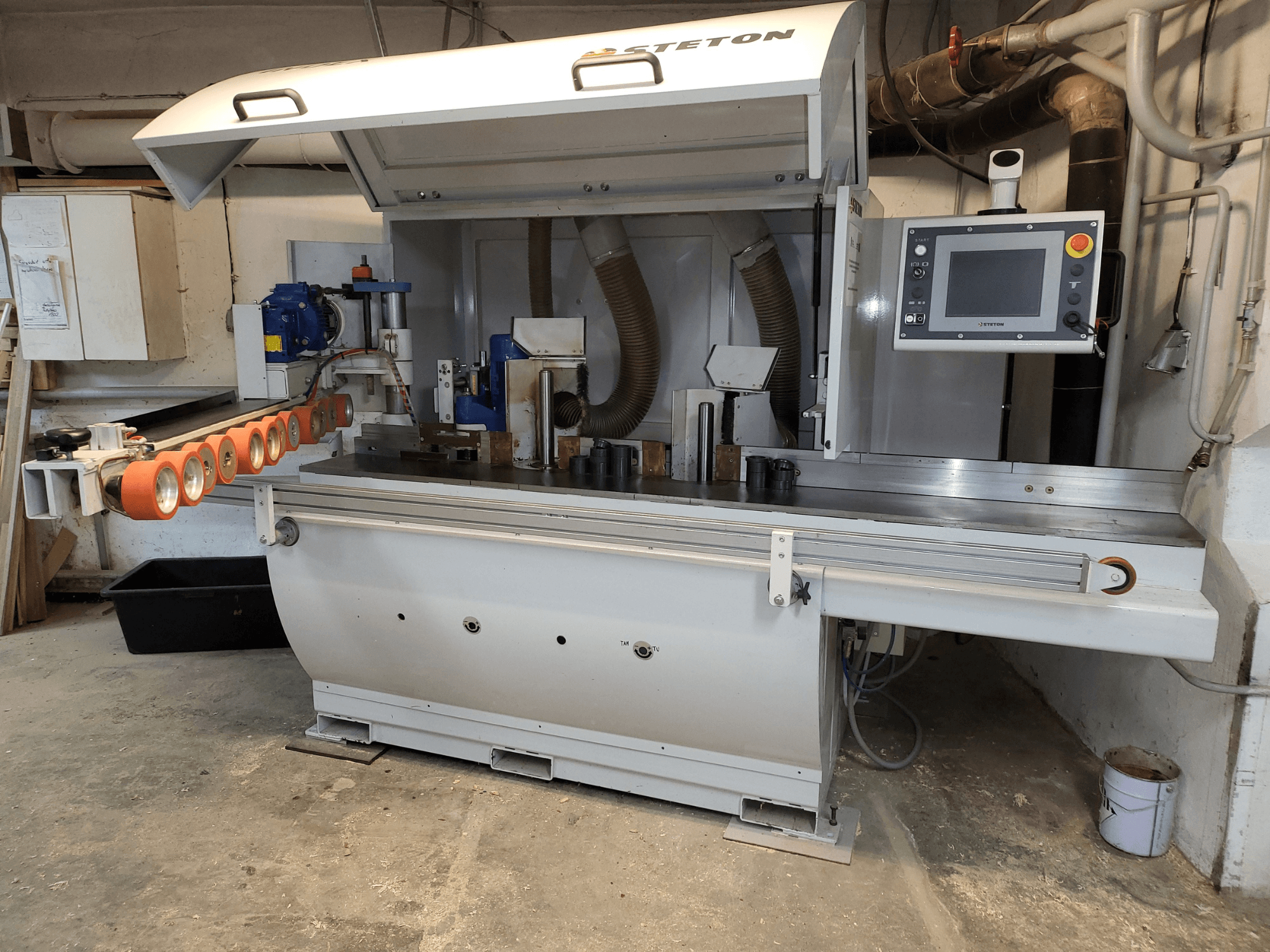 Stettoni puidutöötlemismasina esivaade juhtpaneeli, sööturtorude ja erinevate puidutükkidega laual.