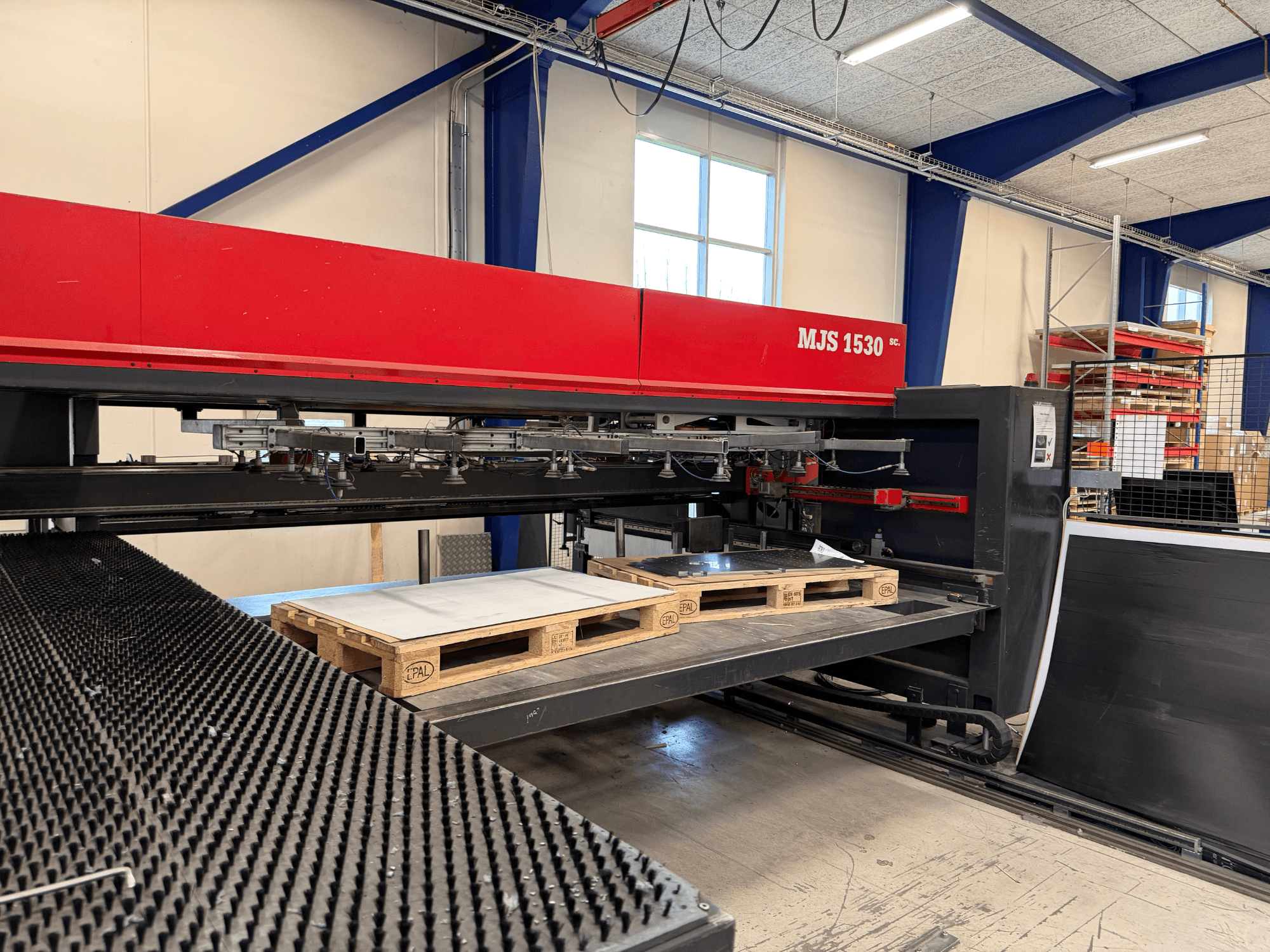 MJS 1530 CNC-tööpink töökojas, esiplaanil, puidust kaubaalus, mis hoiab metallplaati tõstetud platvormil.