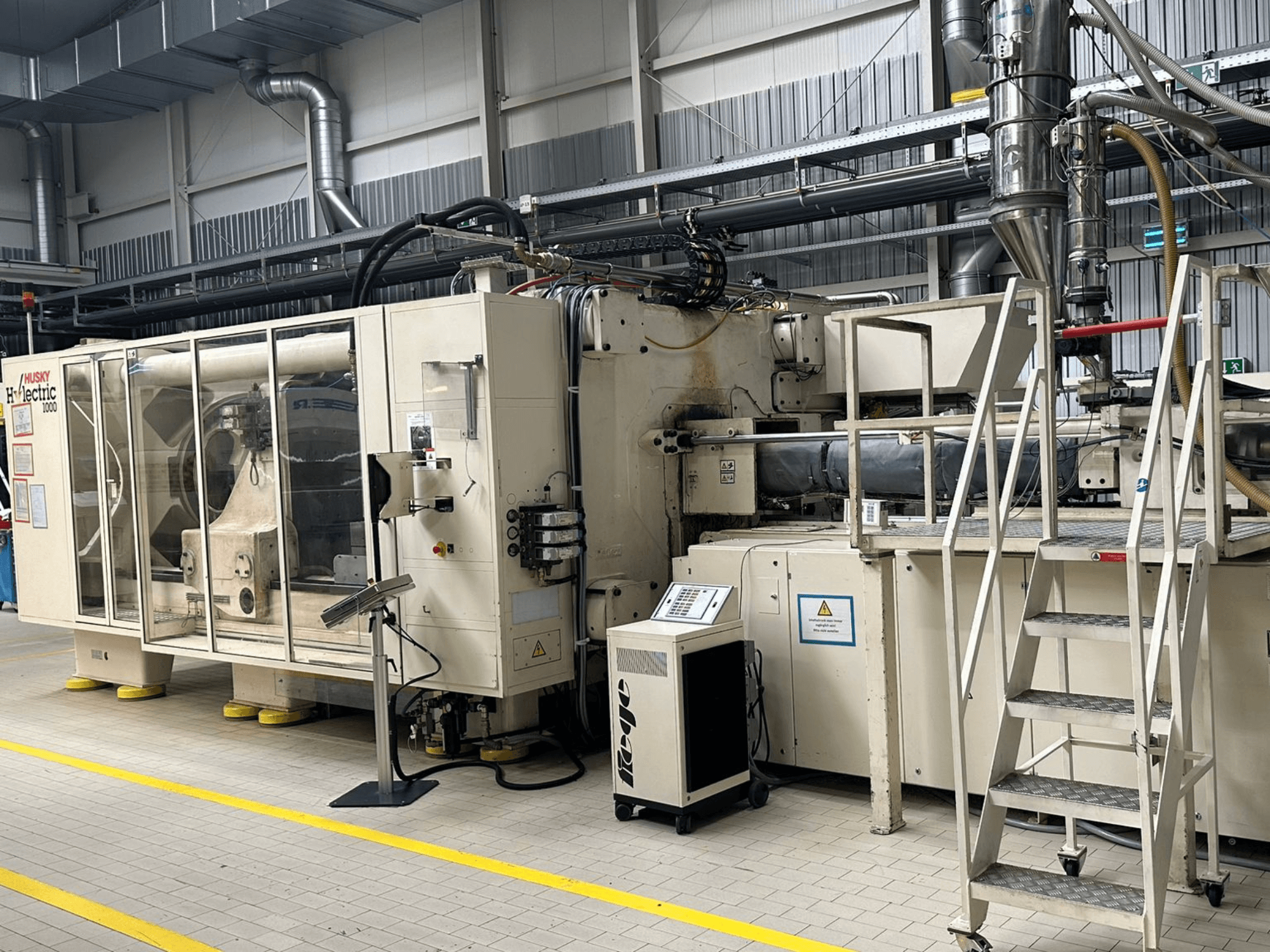 Husky Hylelectric H1000 RS95/80 elektrilise survevalumasina esivaade tehase keskkonnas, millel on näha juhtpaneel ja astmed.