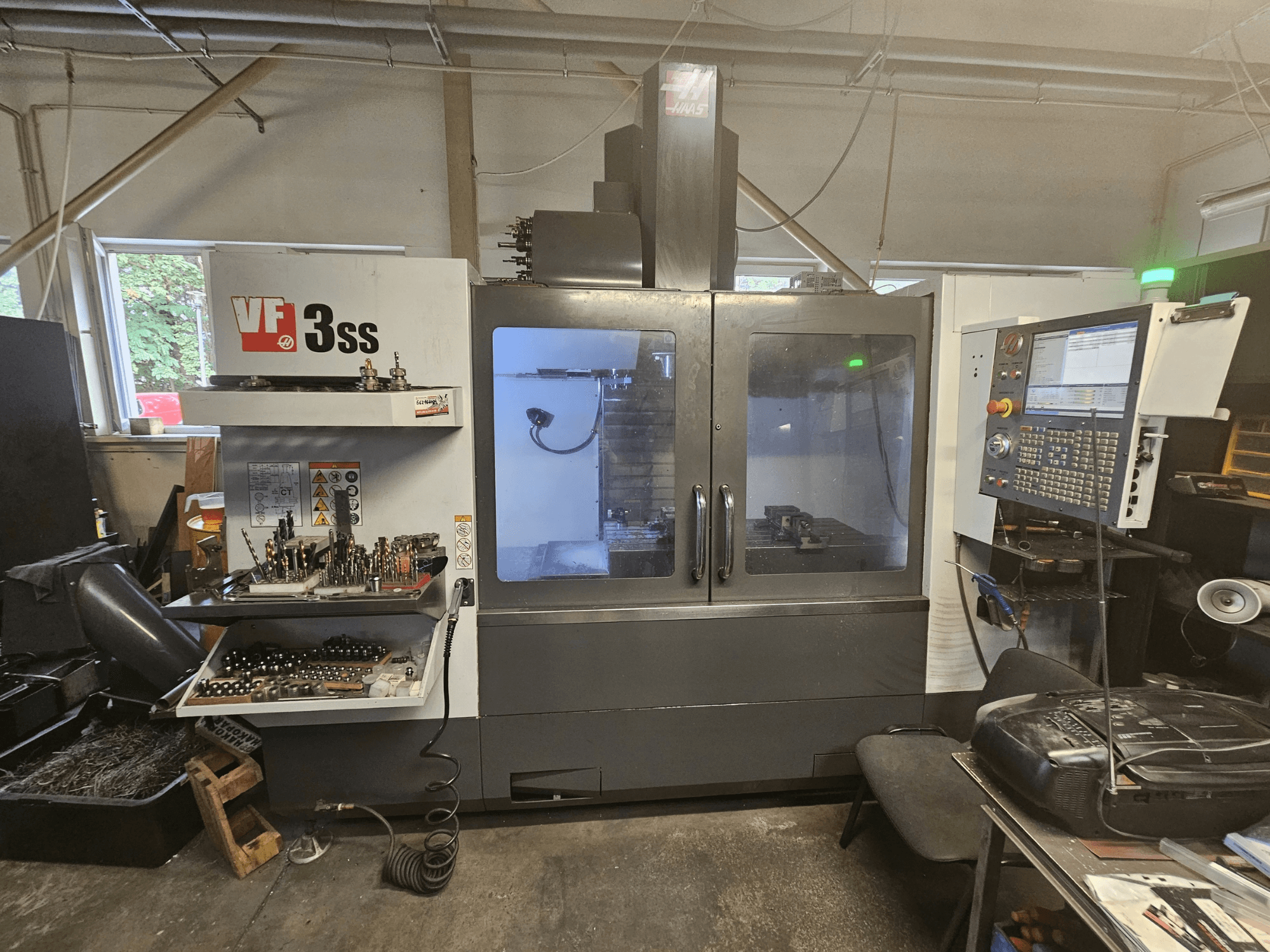 Haas VF-3SS vertikaalne töötlemiskeskus töökodas, esivaade, millel on näha juhtpaneel ja tööriistade hoiuruum.