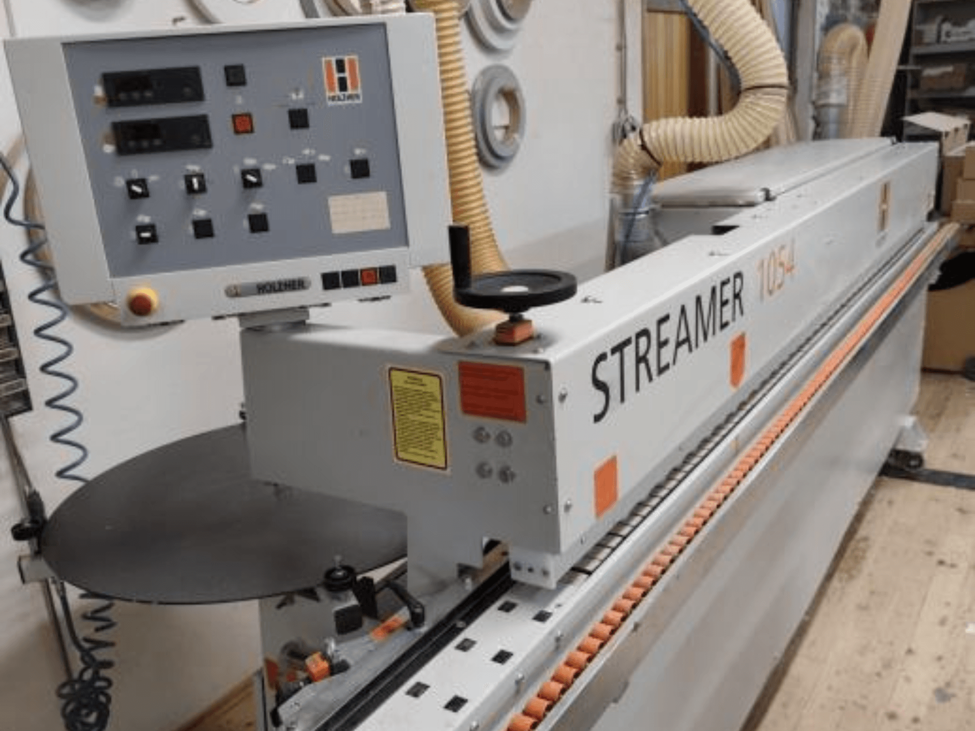 HOLZHER Streamer 1054 servalõikur, külgvaade, kus on näidatud juhtpaneel ja etteandesüsteem töökoja taustal.