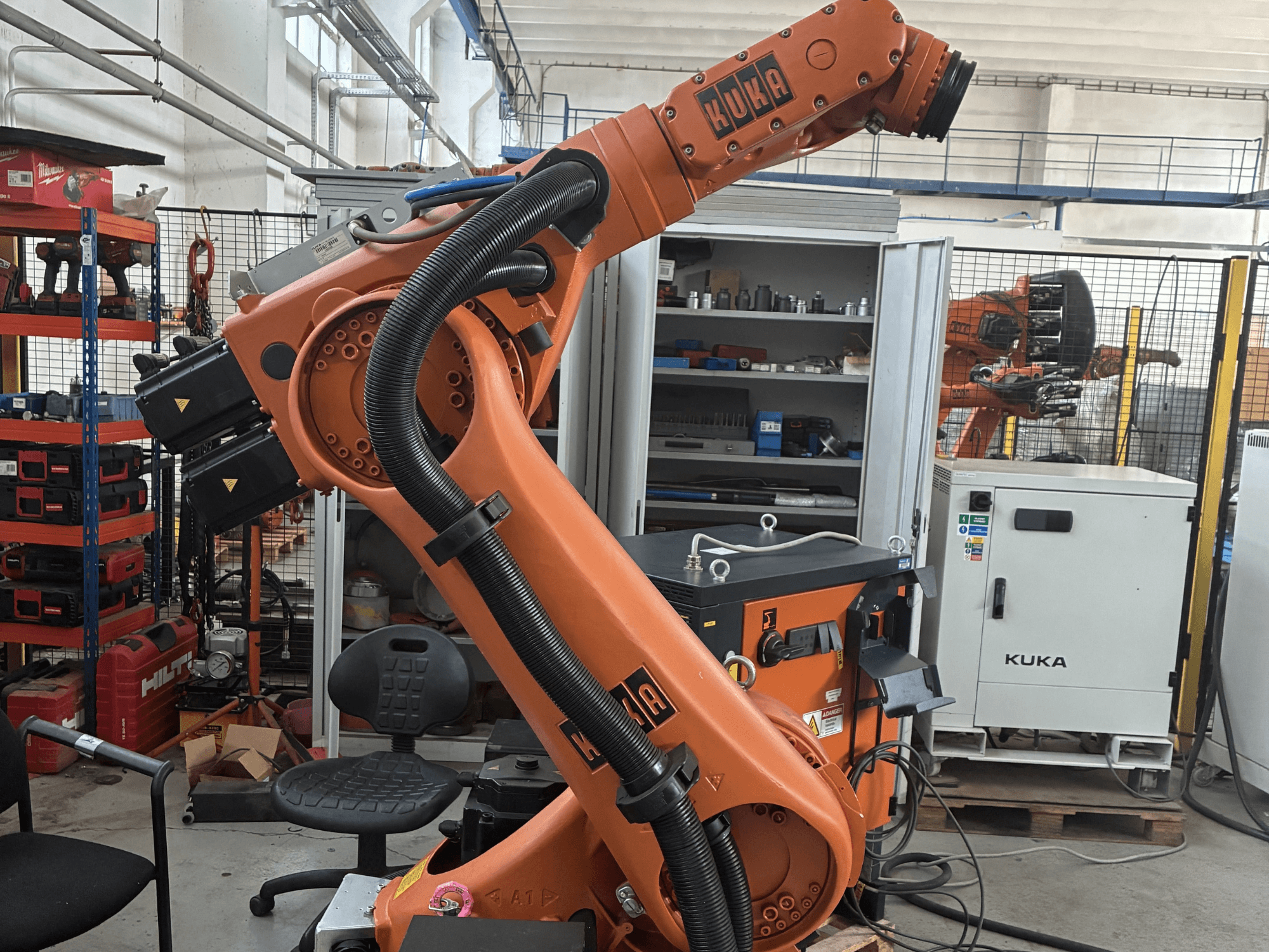 KUKA KR30-3 robotkäsi tööstuslikus keskkonnas, külgvaates on näha kaablid ja juhtimisseadmed, taustal tööriistad ja riiulid.