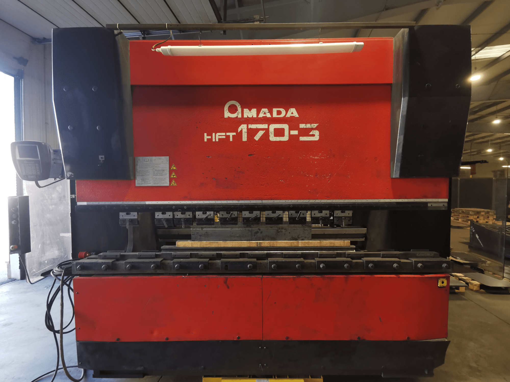 Punane Amada HFT 170-3 presspink eespoolt, kus on näha juhtpaneel, painutusvahendid ja tööpind.
